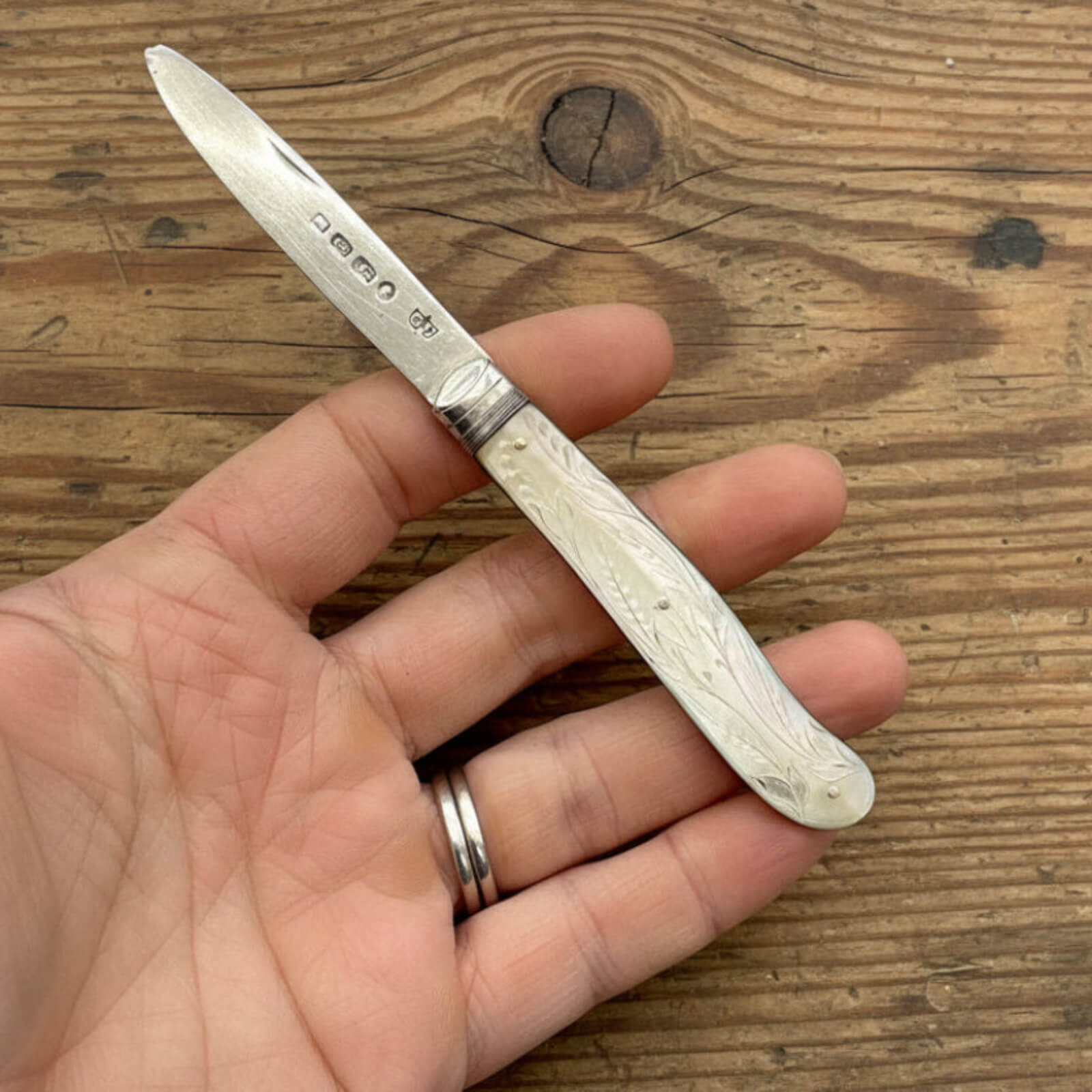 Hand holding a fruit knife with a decorative handle on a wooden surface