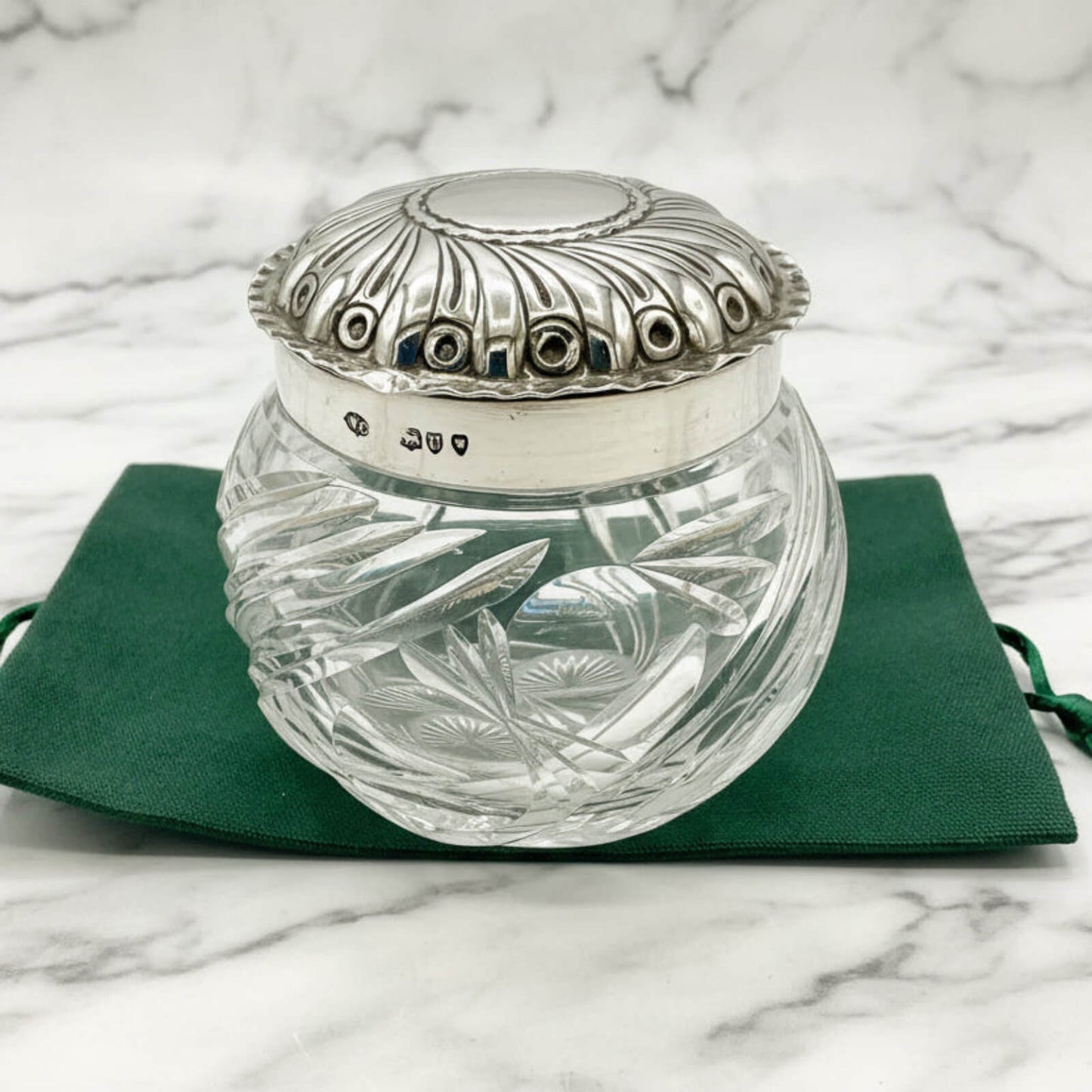 Decorative glass jar with silver lid on a green cloth against a marble background