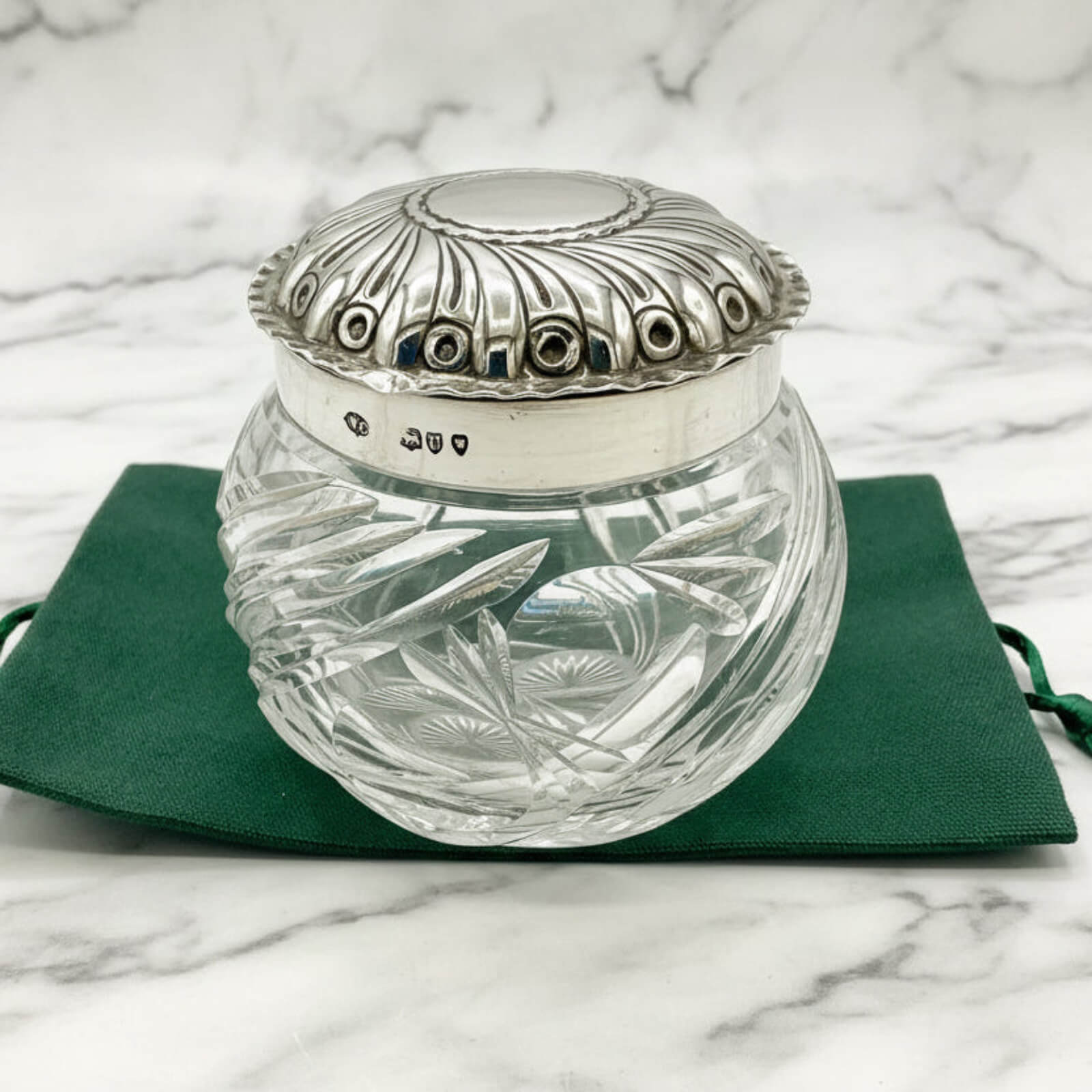Decorative glass jar with silver lid on a green cloth against a marble background