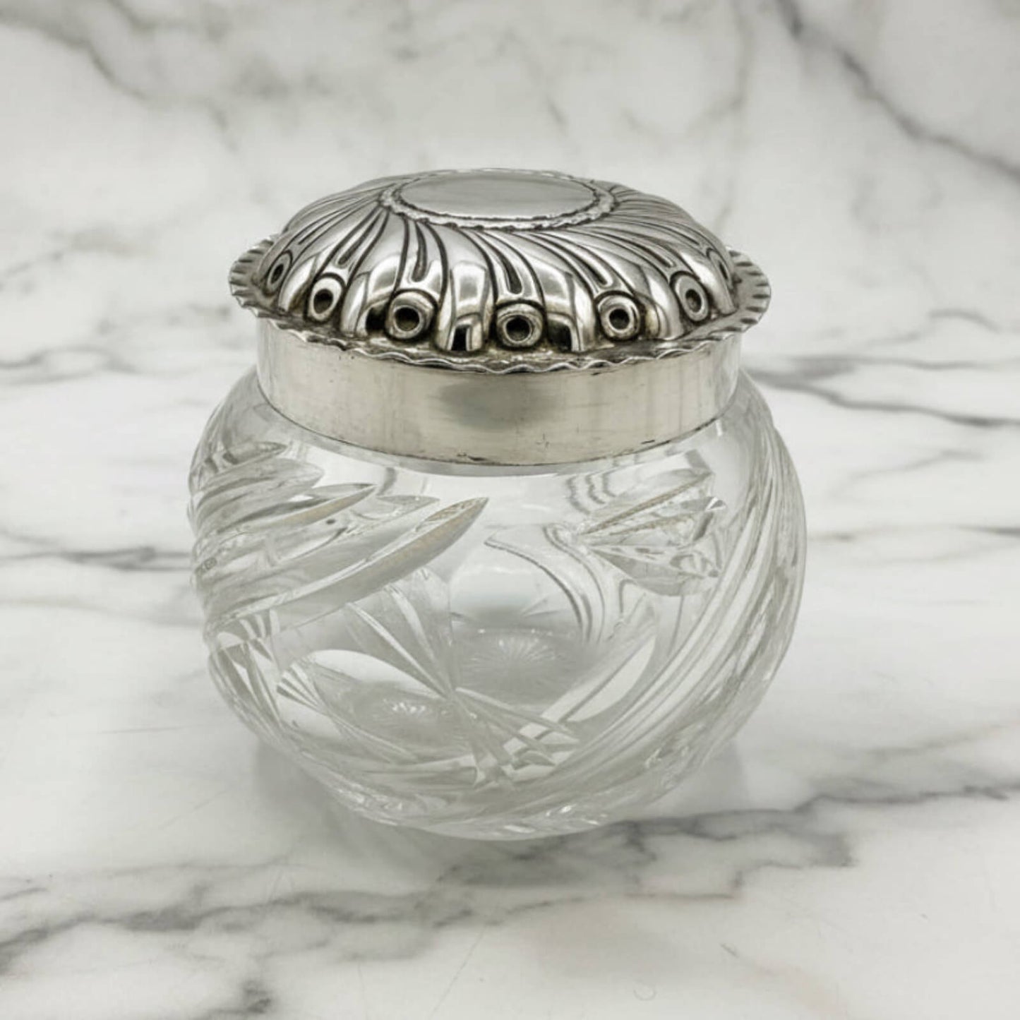 Decorative glass jar with silver lid on a marble surface