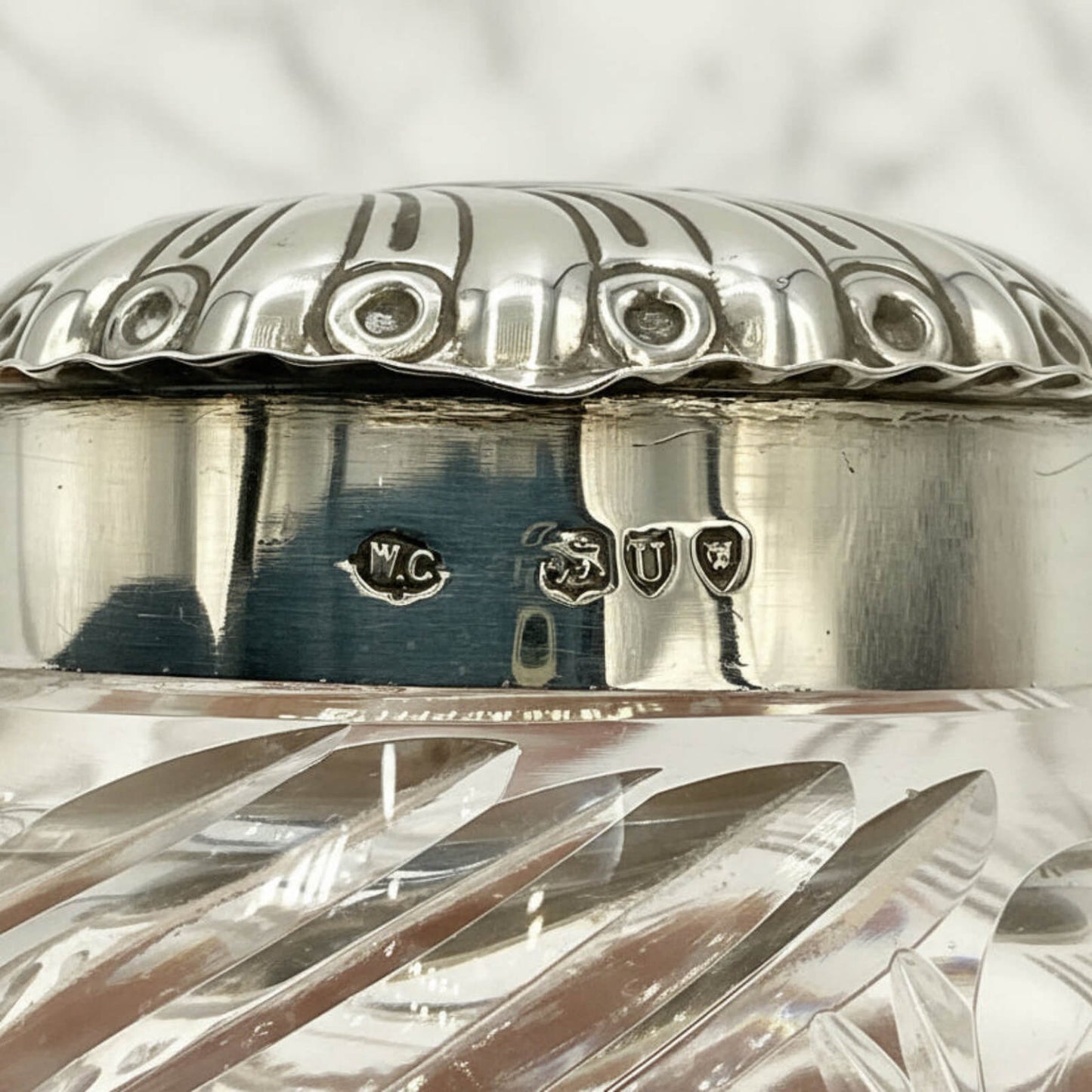 Close-up of a silver and crystal container with engraved hallmarks on a textured gray background