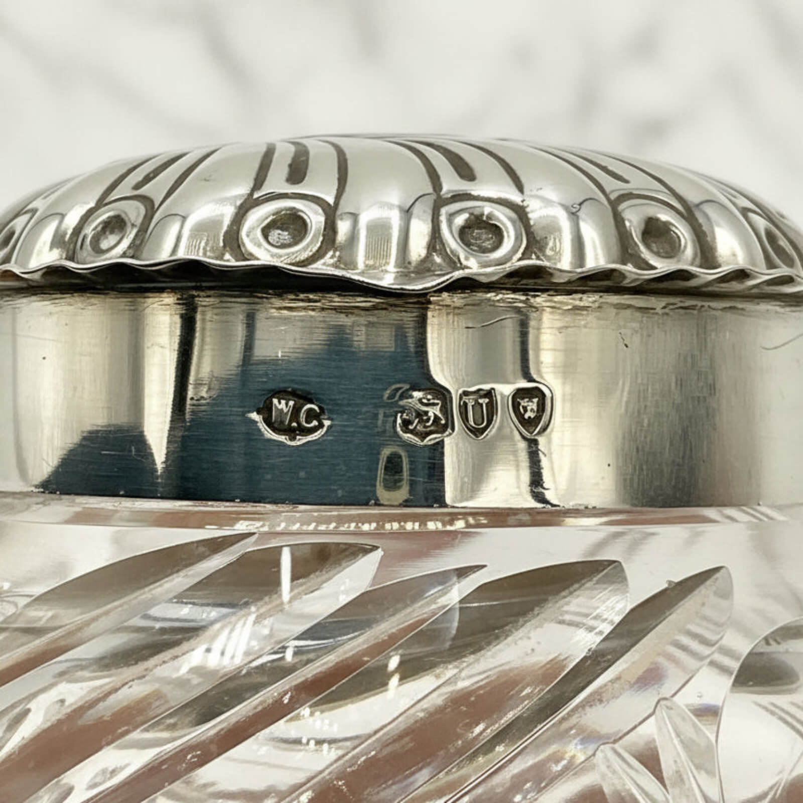 Close-up of a silver and crystal container with engraved hallmarks on a textured gray background