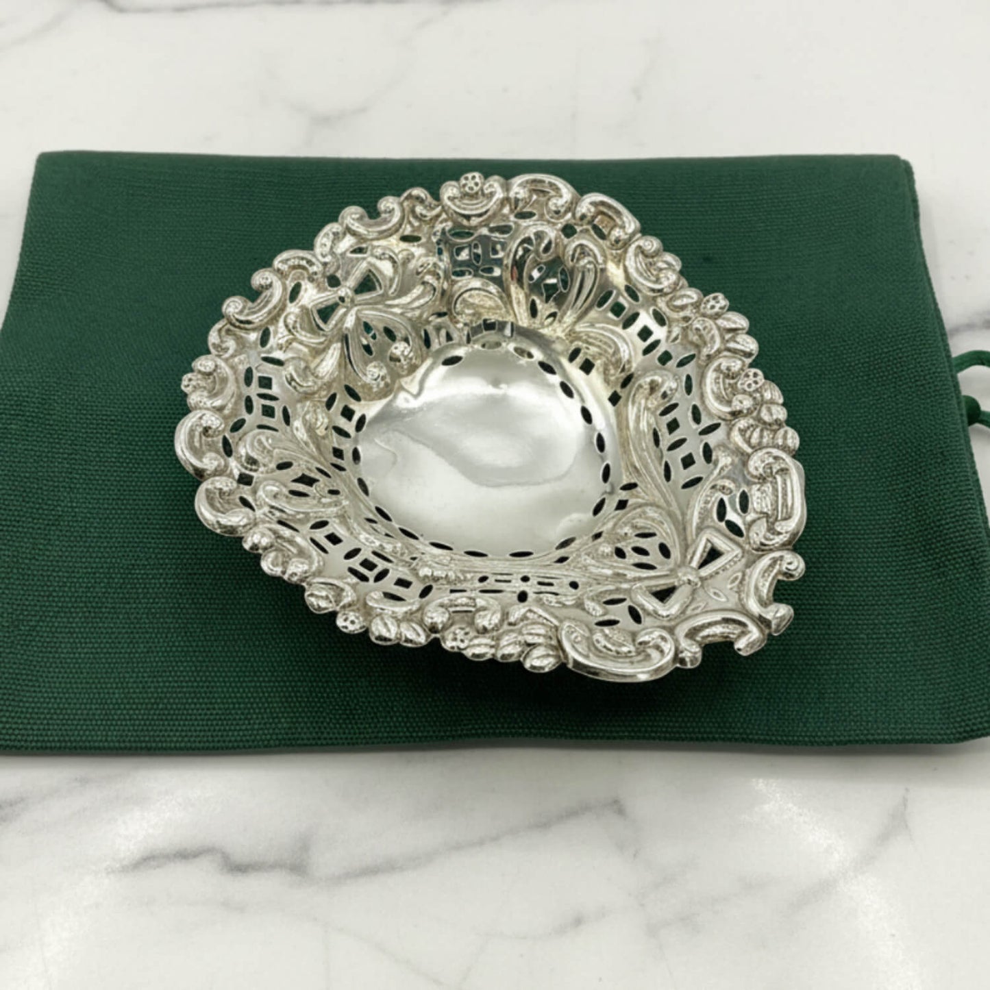 Decorative silver bowl on a green fabric bag and marble background