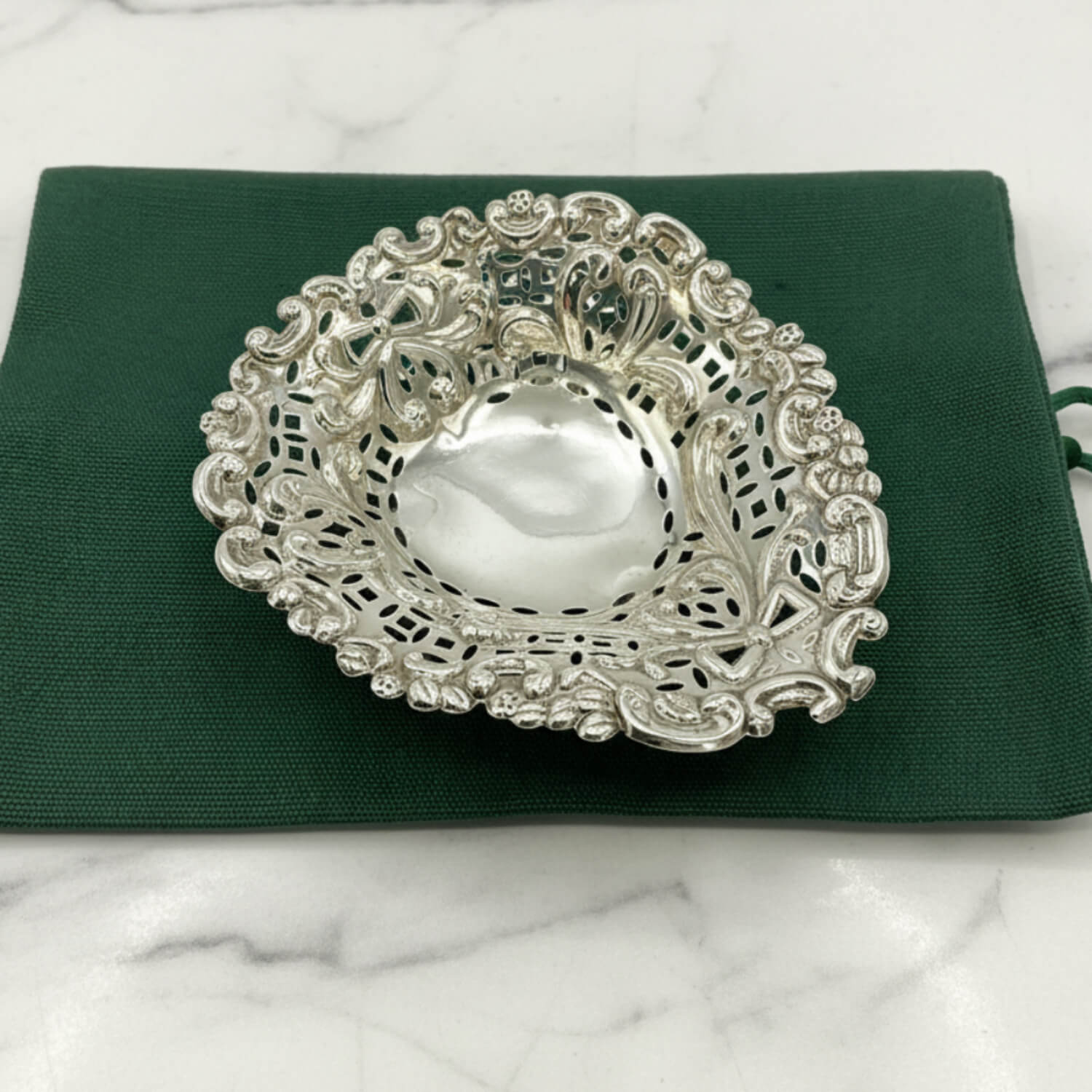 Decorative silver bowl on a green fabric bag and marble background