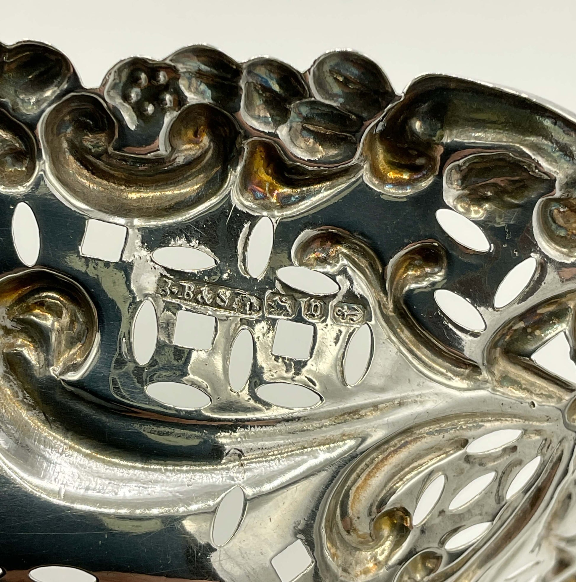 Close-up of ornate silverware bowl with engraved hallmarks and makers mark. .