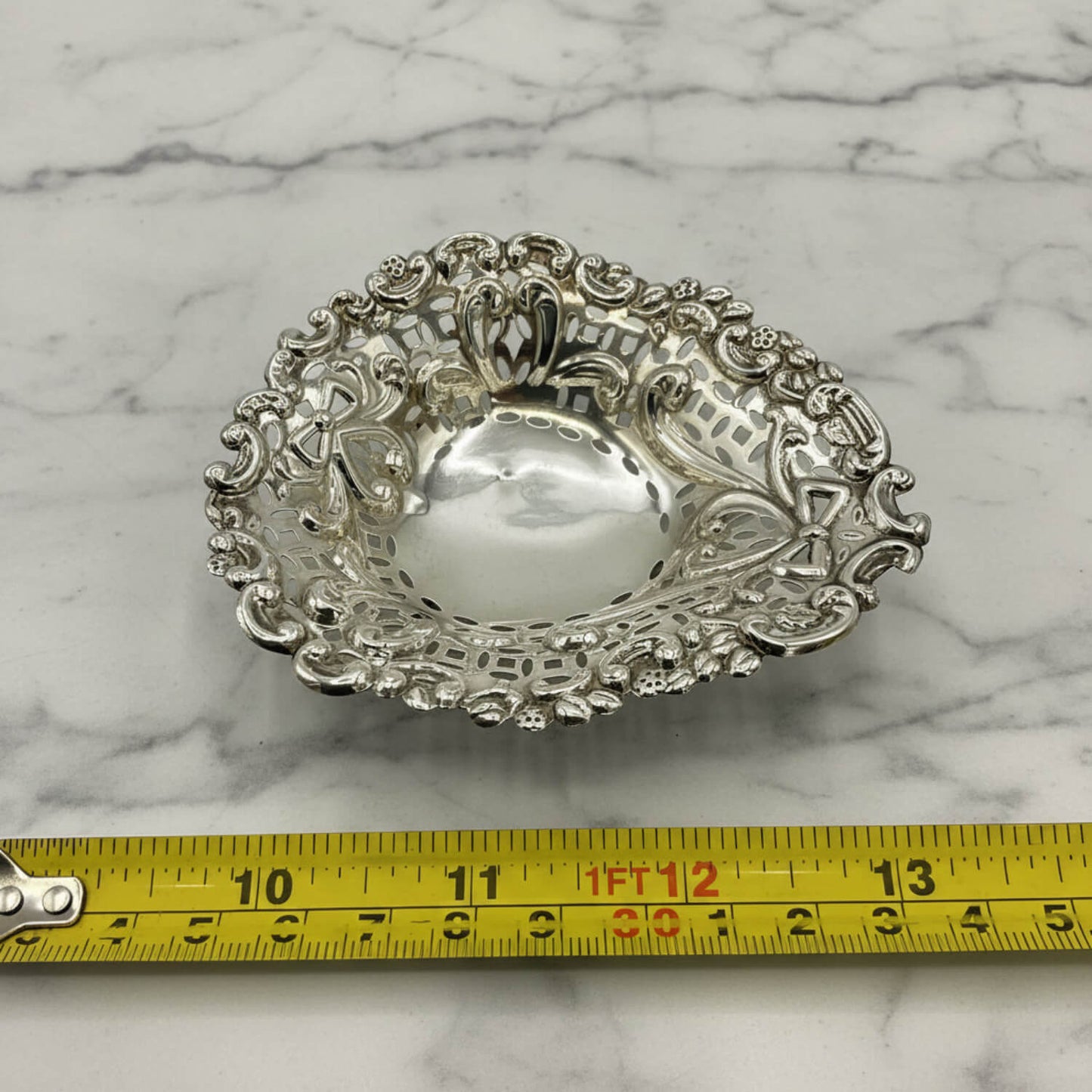 Decorative silver bowl on a marble surface with a tape measure for scale.