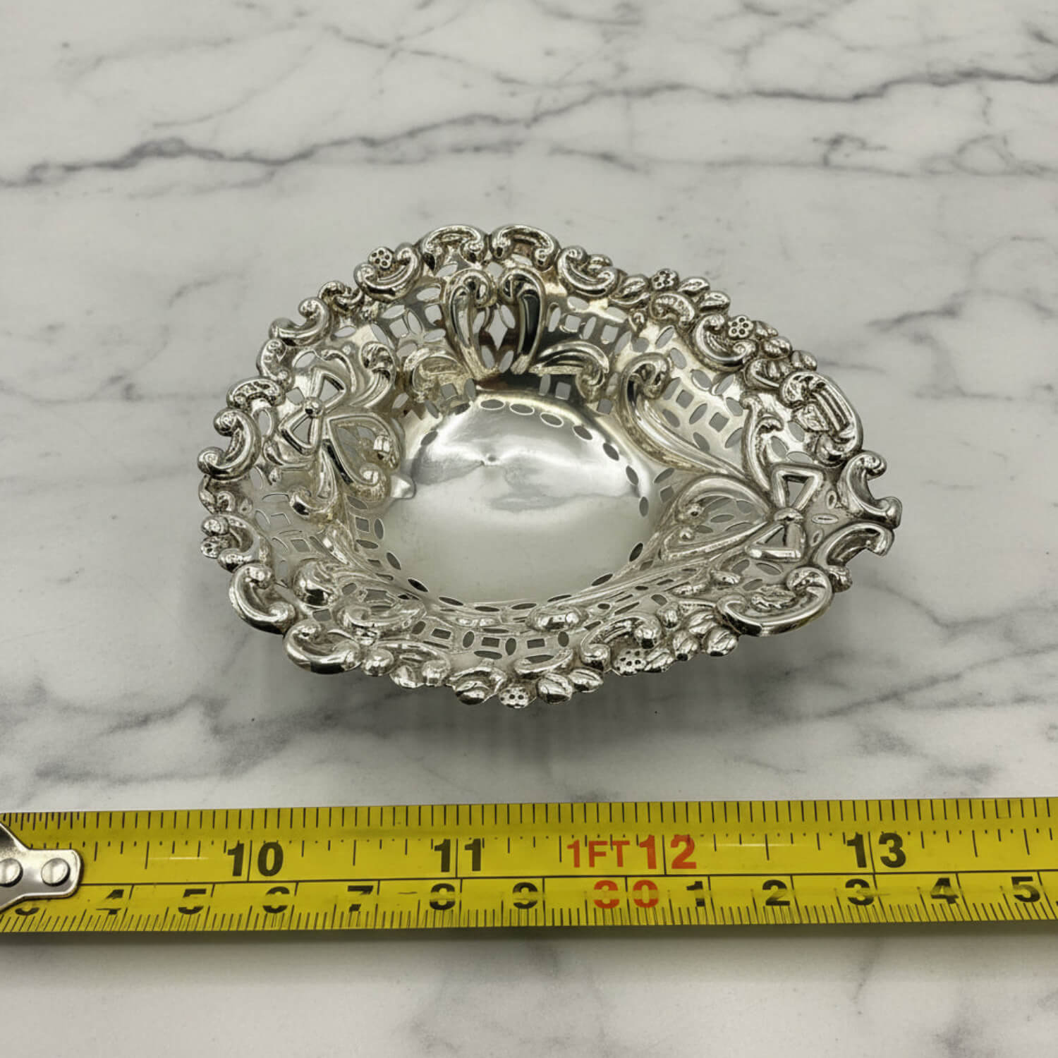 Decorative silver bowl on a marble surface with a tape measure for scale.