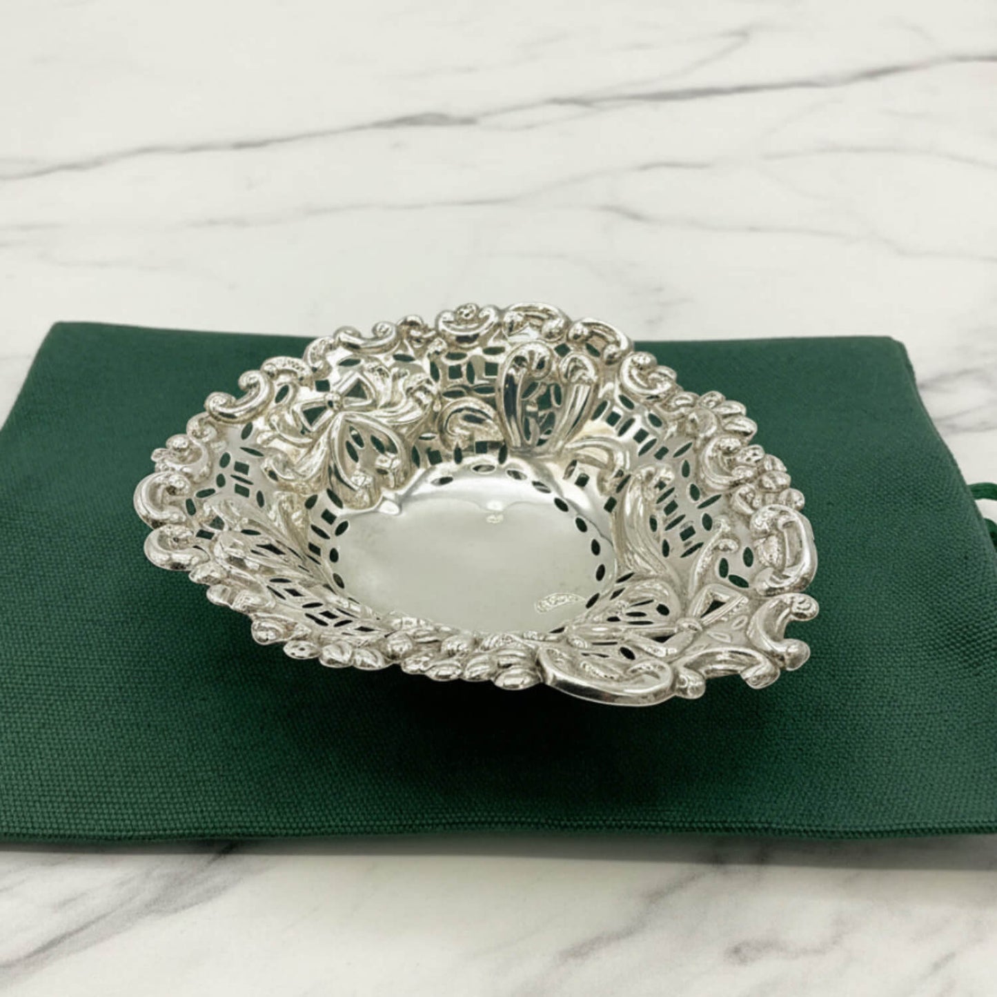 Decorative silver bowl on a green cloth bag with a marble background