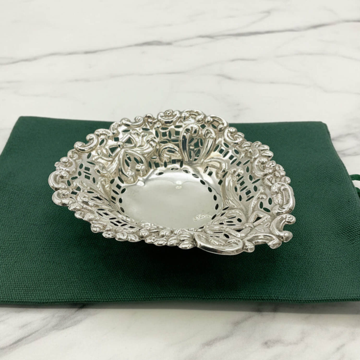 Decorative silver bowl on a green cloth bag with a marble background
