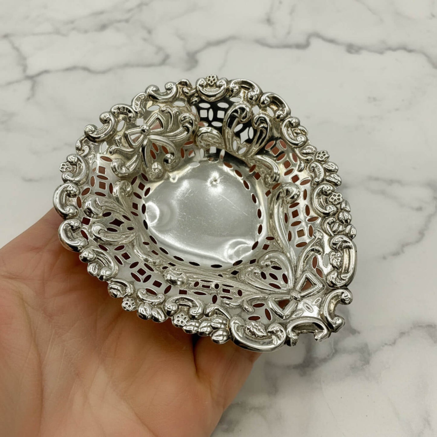 Decorative silver dish held in a hand against a marble background