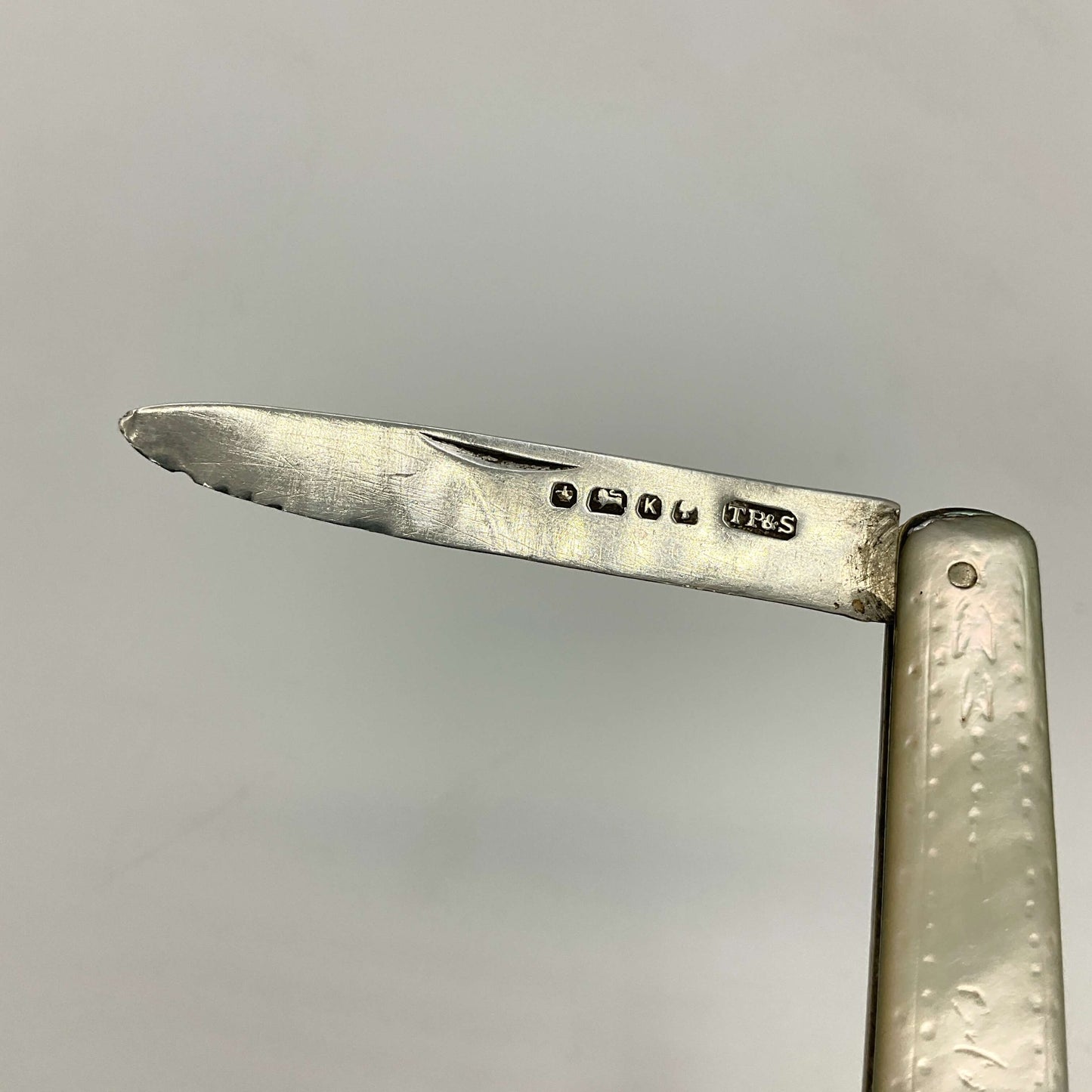 Close-up of a silver fruit knife blade with engraved hallmarks on a gray background