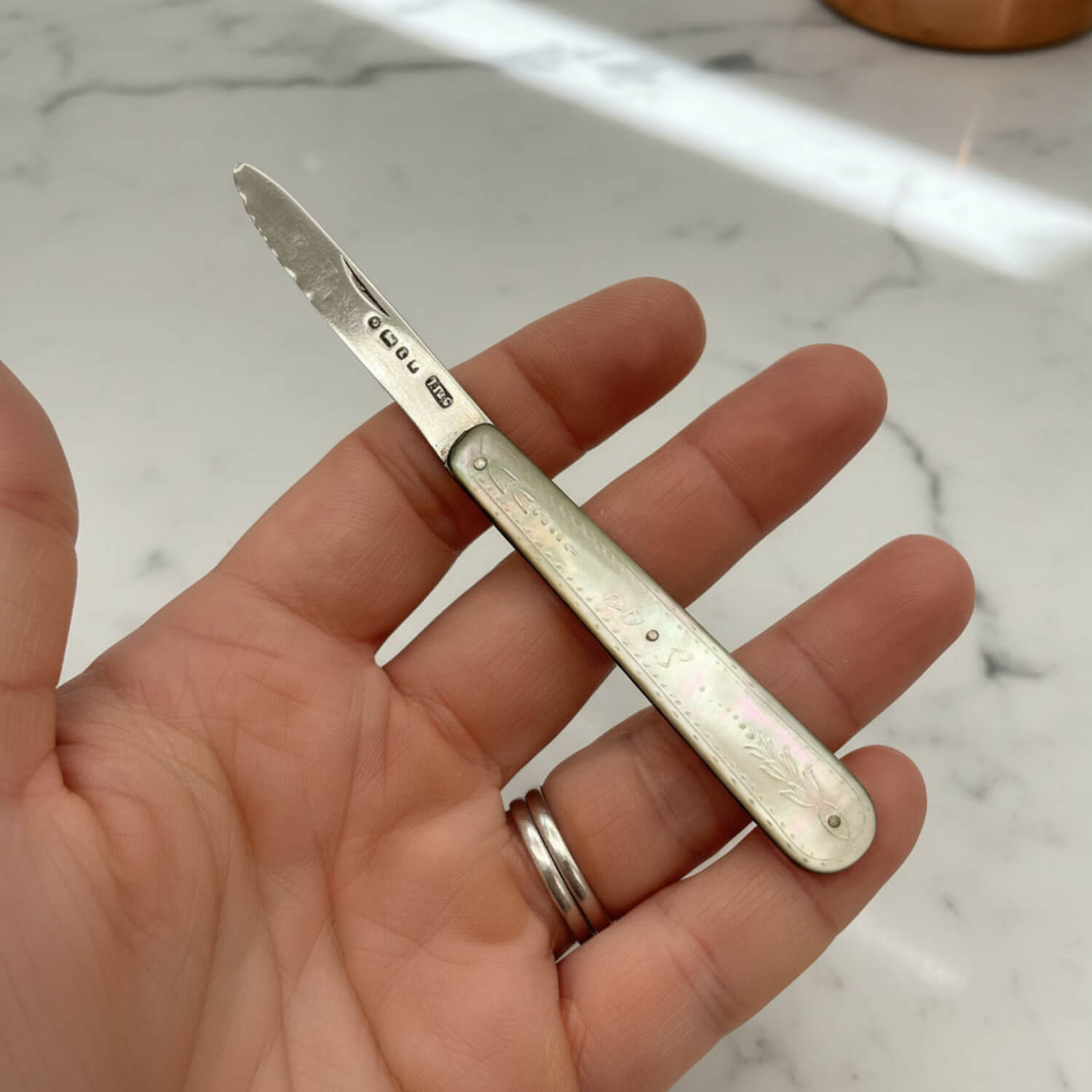 Hand holding a silver fruit knife with engraved details on a marble surface