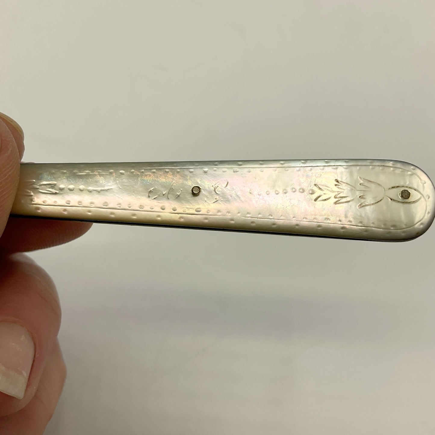 Silver fruit knife handle held by a hand against a plain background