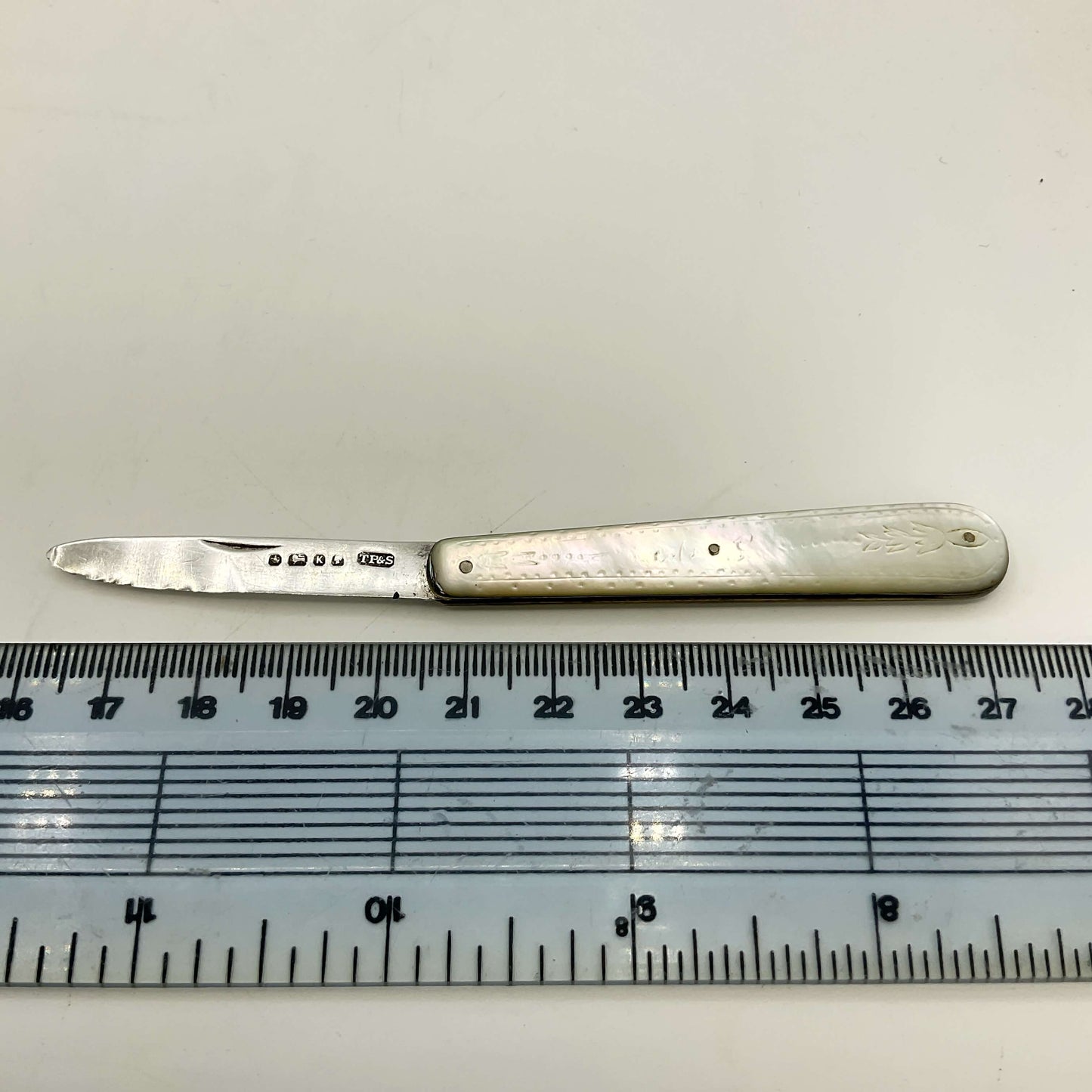Silver knife with a decorative handle on a white background, next to a ruler for scale.