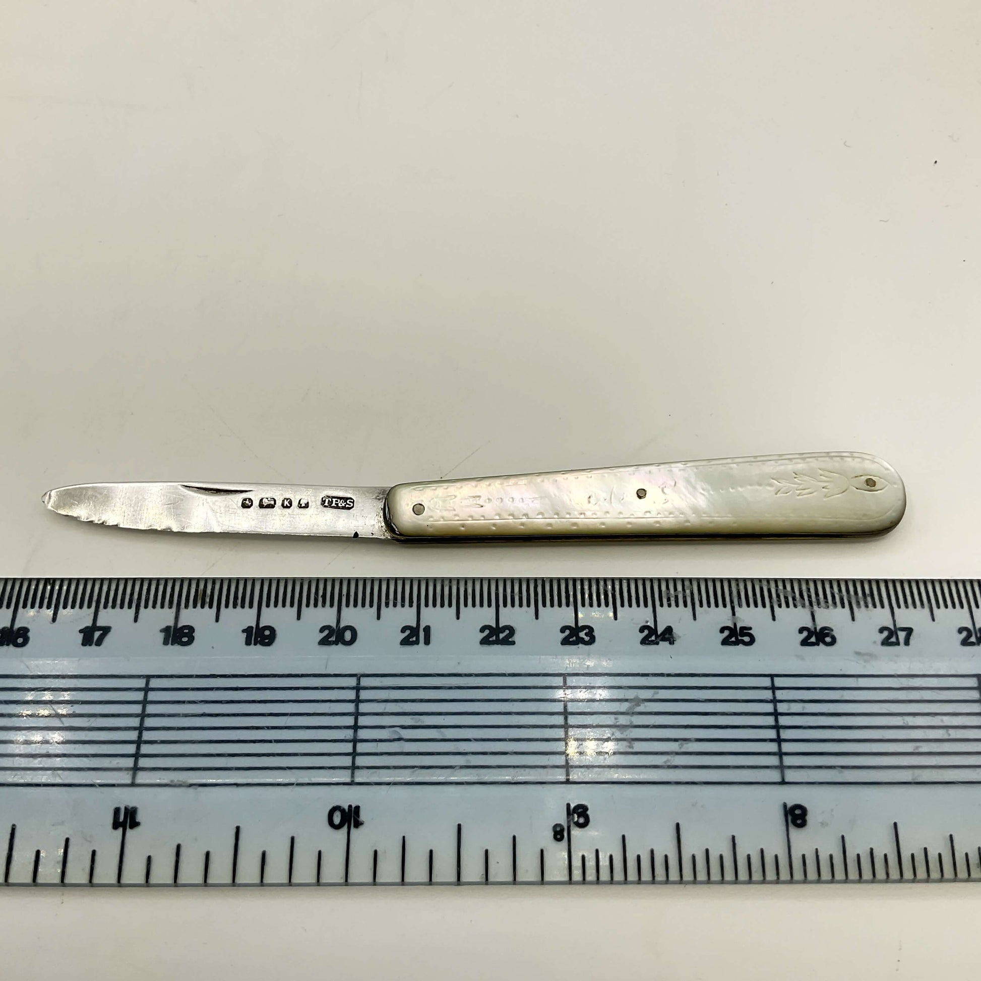 Silver knife with a decorative handle on a white background, next to a ruler for scale.