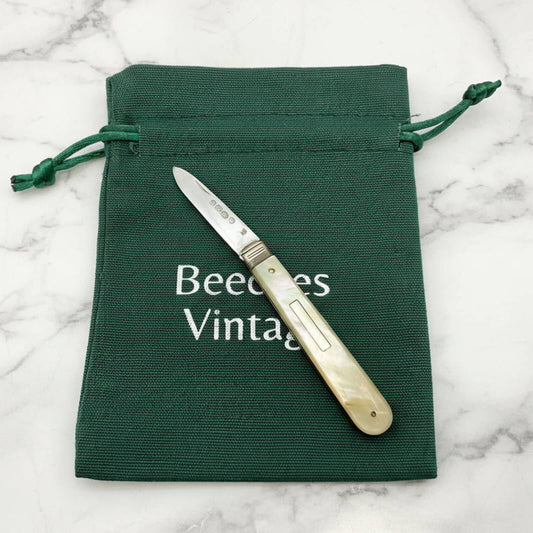Foldable knife on a green drawstring bag with 'Beeches Vintage' text on a marble background
