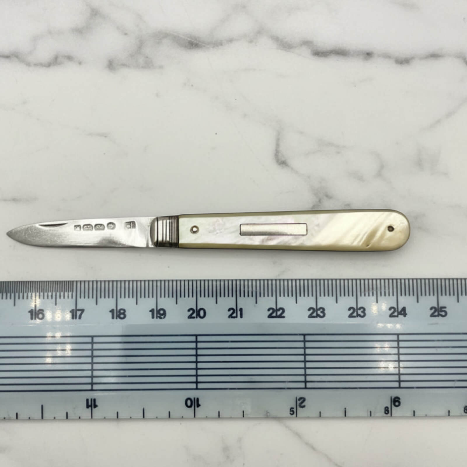 Knife with a decorative handle on a marble surface next to a ruler for scale.