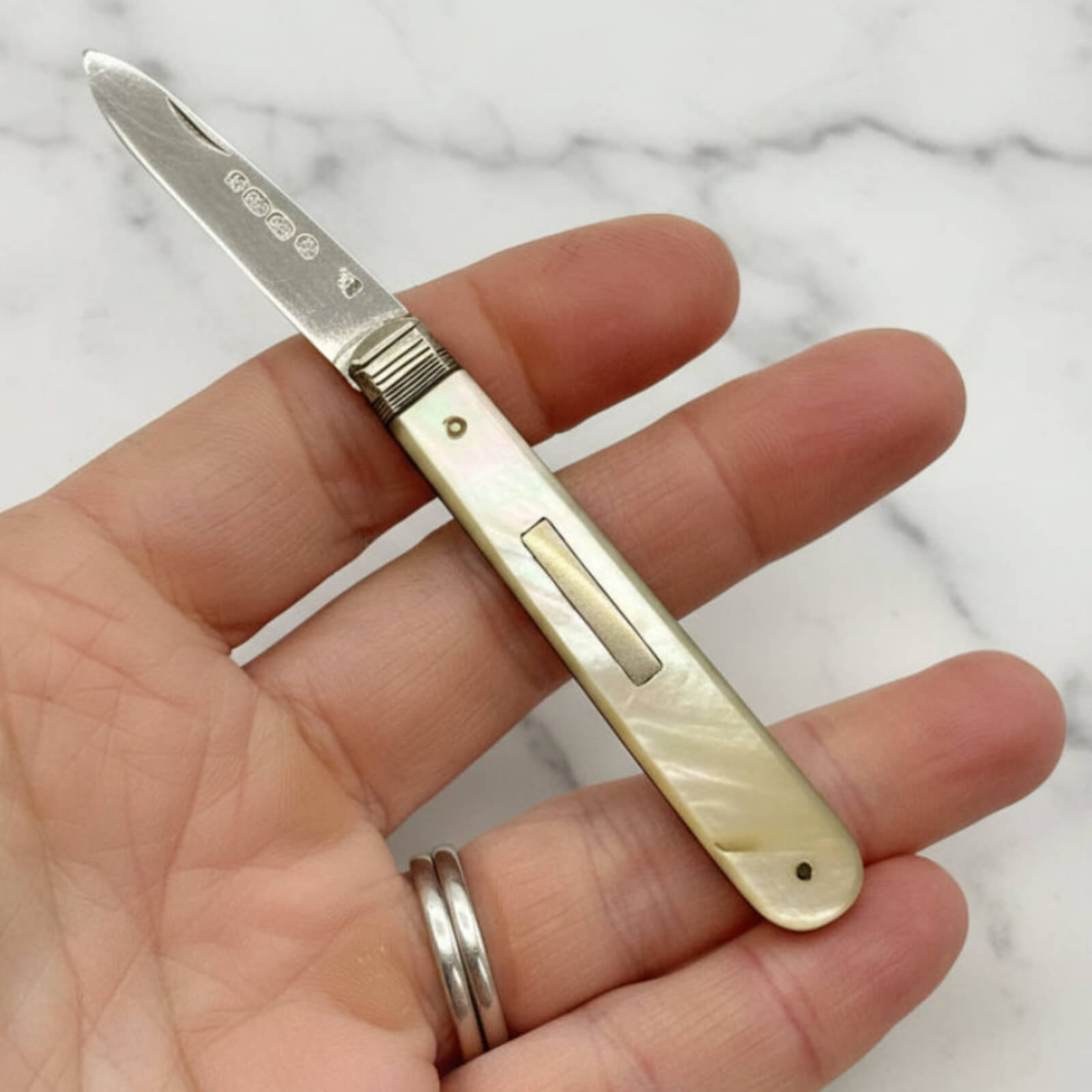Small pocket knife held in a hand with a marble background