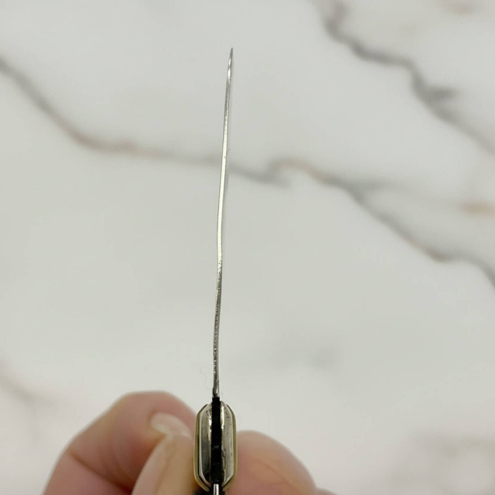 Close-up of a fruit knife blade held between fingers against a marble background