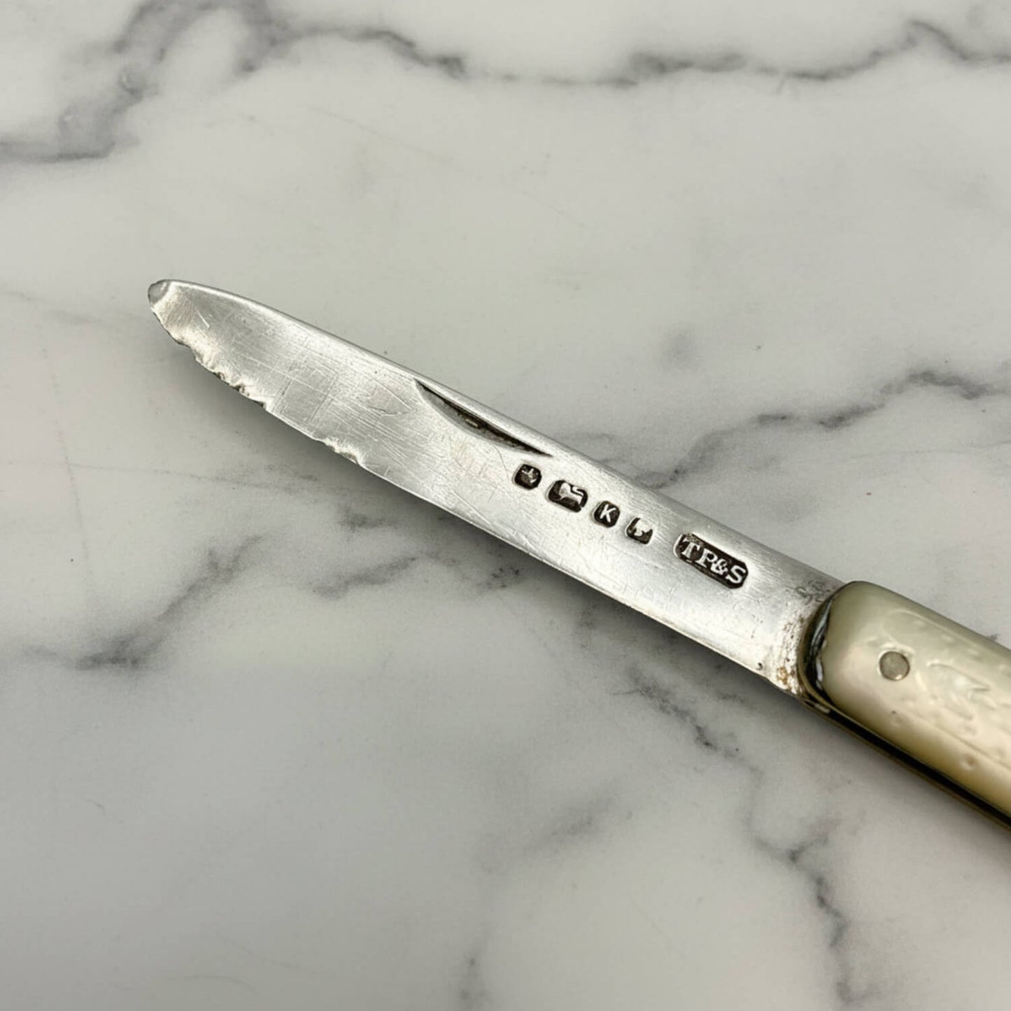 Antique fruit knife with engraved hallmark details on a marble surface