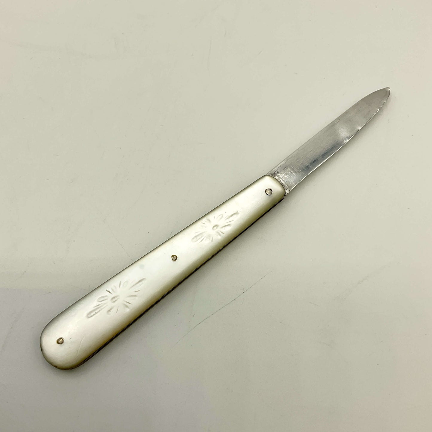 Silver fruit knife with engraved handle on a light gray background
