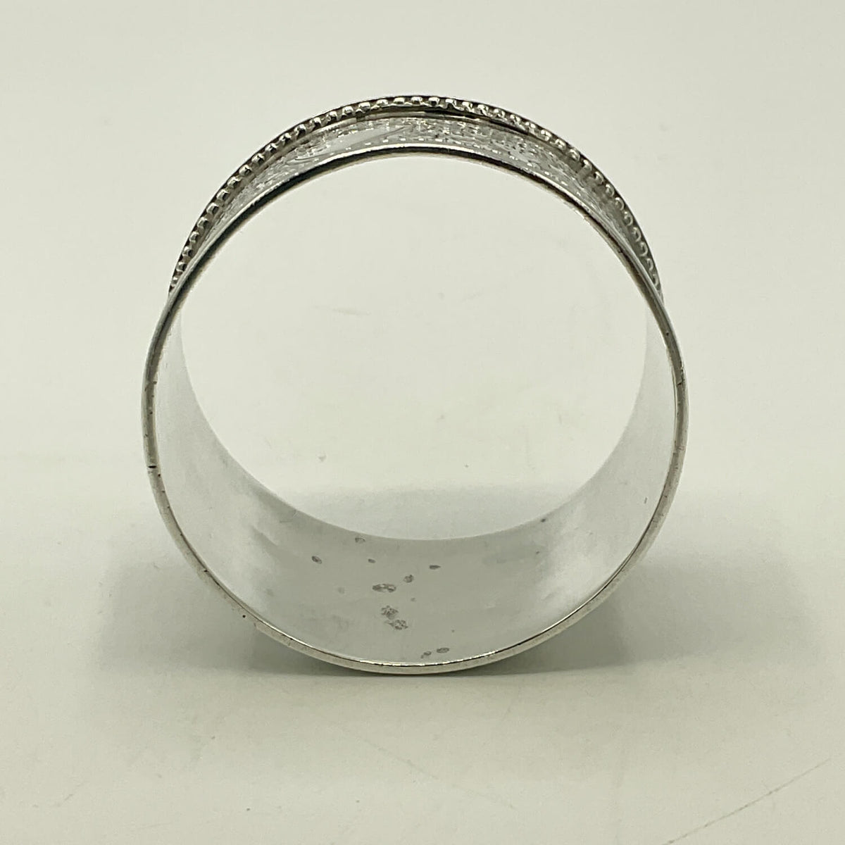 A silver napkin ring with a textured beaded outer edge and a smooth interior, photographed on a plain light background.
