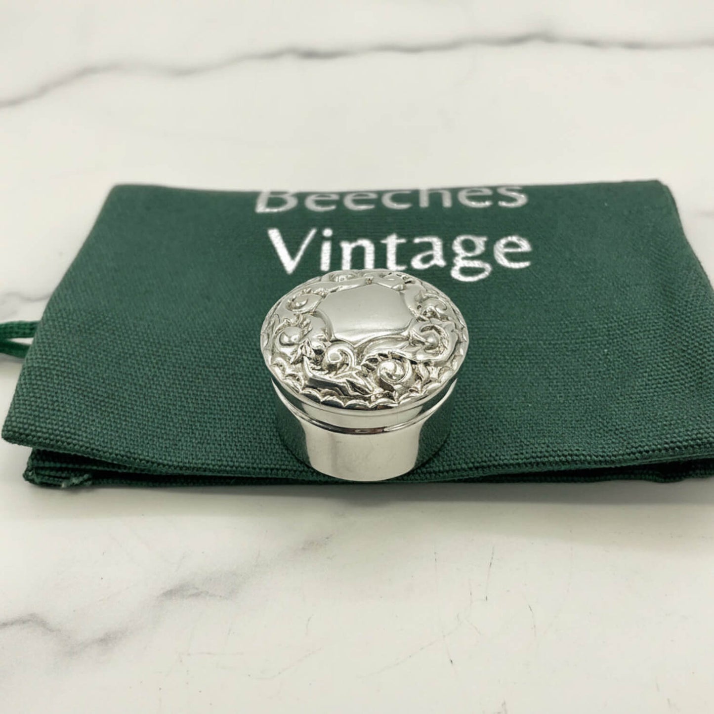 Silver decorative pill box on a green bag with 'Beeches Vintage' branding.