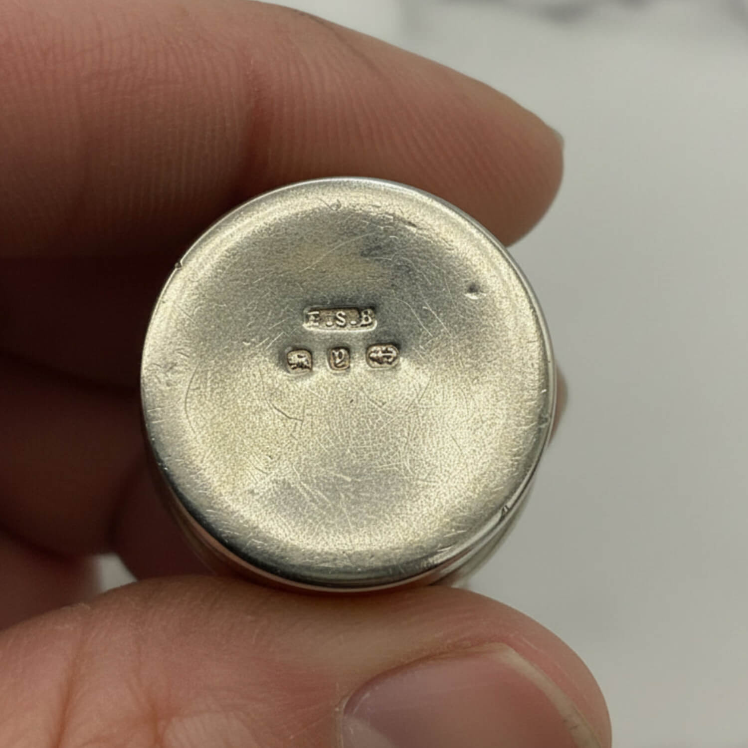 Silver pill box held between fingers with visible hallmarking on a white background