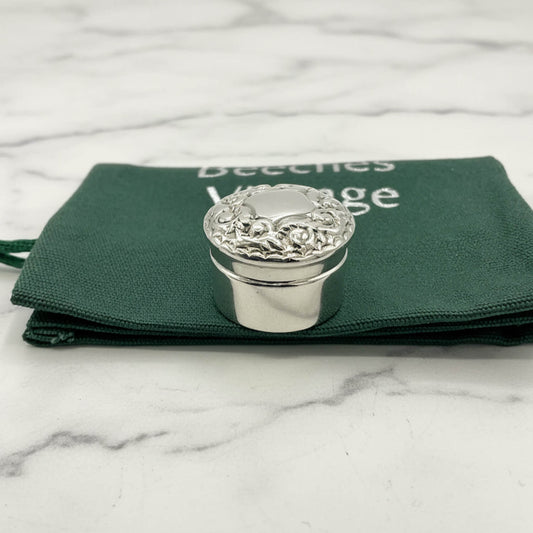 Silver decorative pill box on a green fabric bag with a marble background