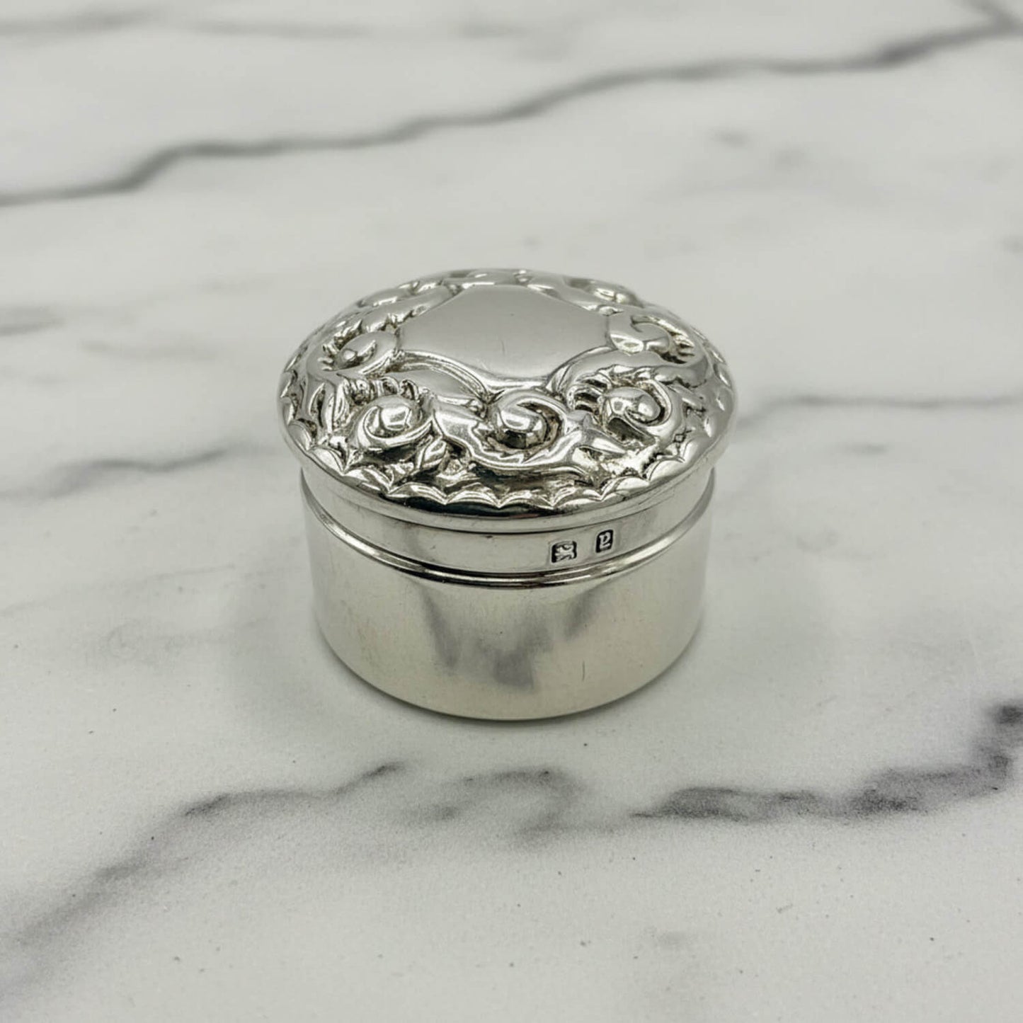 Decorative silver box with floral patterns on a marble surface