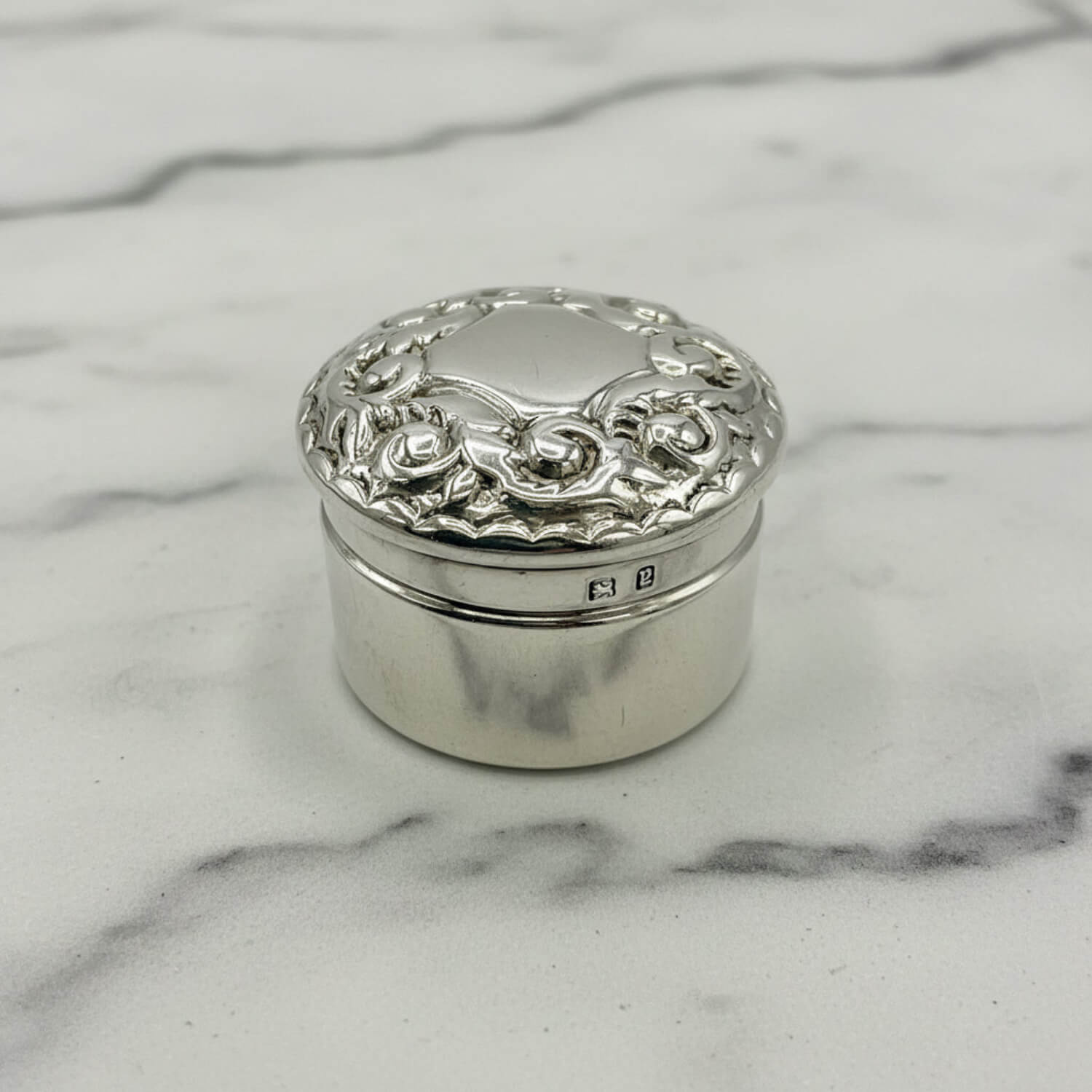 Decorative silver box with floral patterns on a marble surface