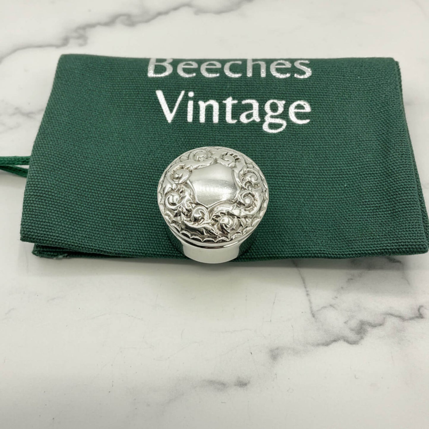 Silver decorative pill box on a green Beeches Vintage cloth bag background