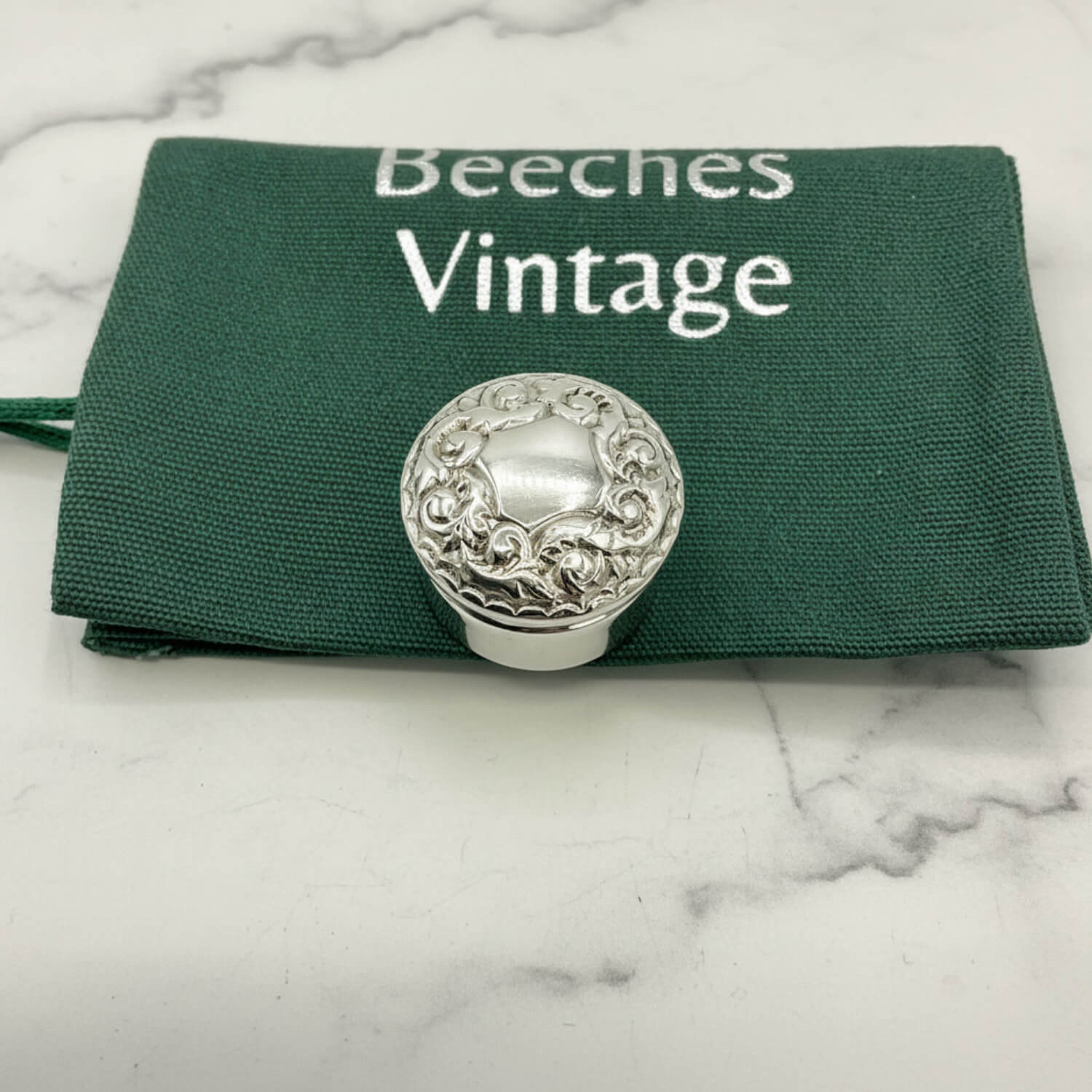 Silver decorative pill box on a green Beeches Vintage cloth bag background