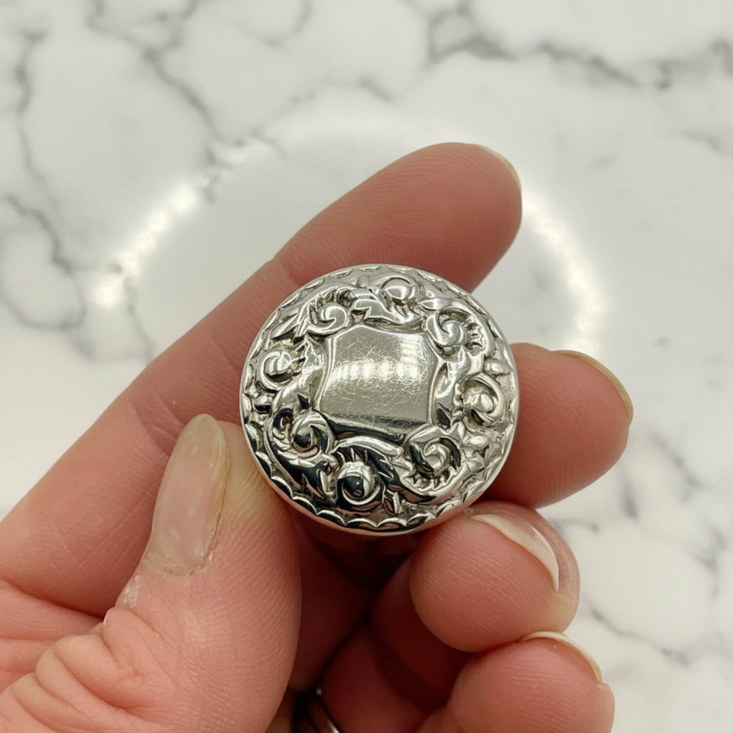 Silver decorative pill box held between fingers against a marble background