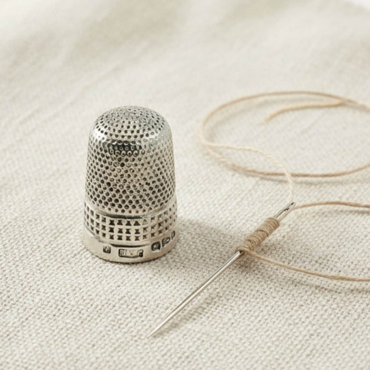 Silver thimble and needle with thread on a textured fabric background