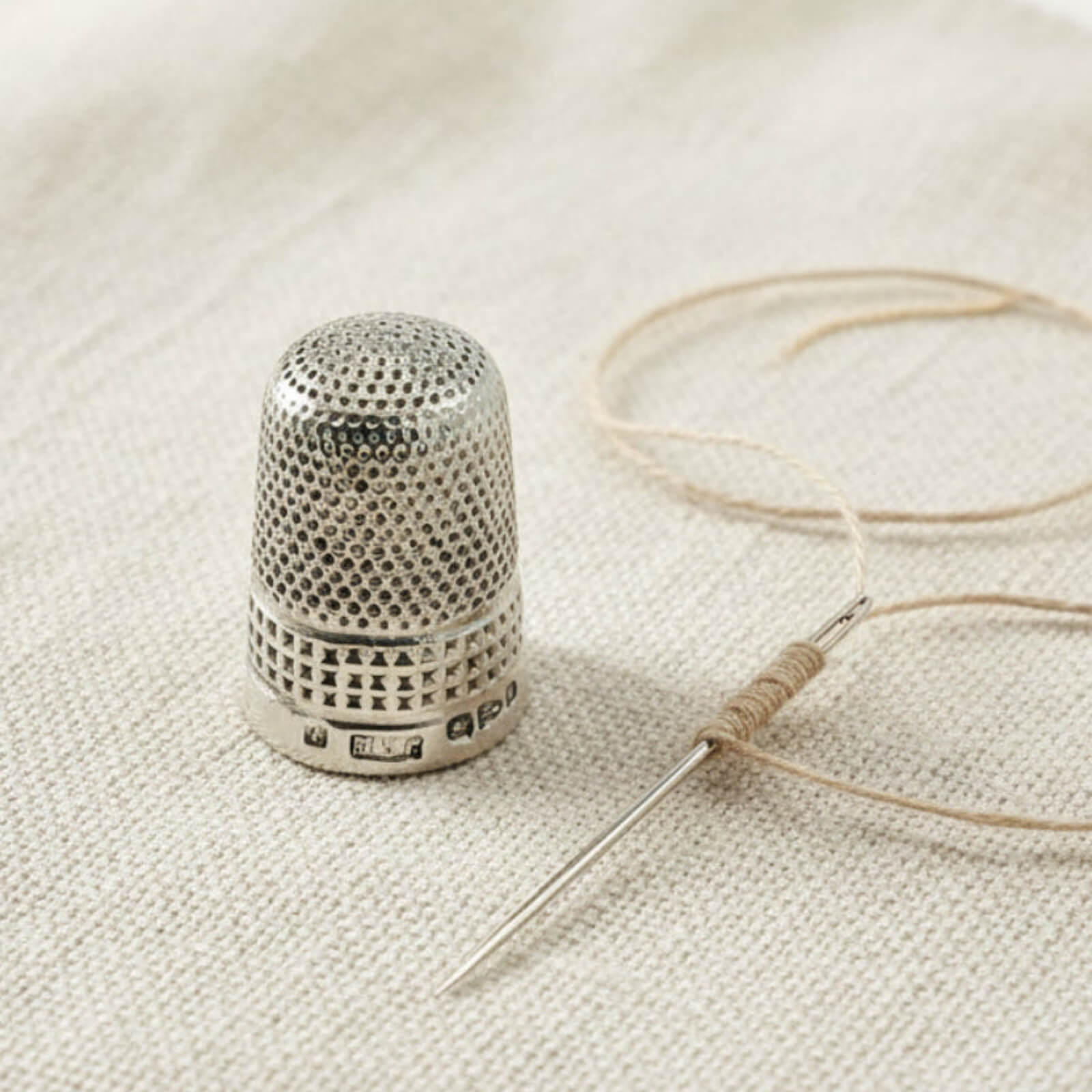 Silver thimble and needle with thread on a textured fabric background