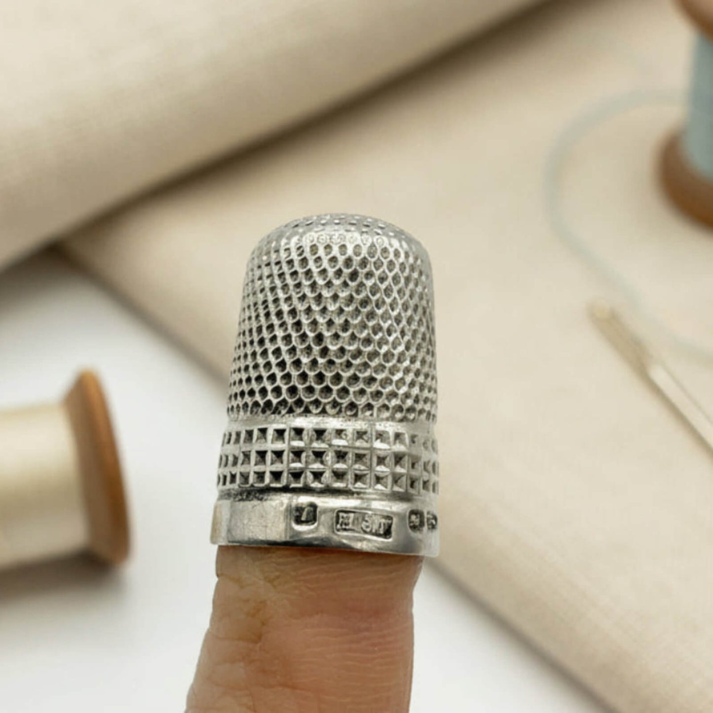 Silver thimble on a finger with sewing materials in the background