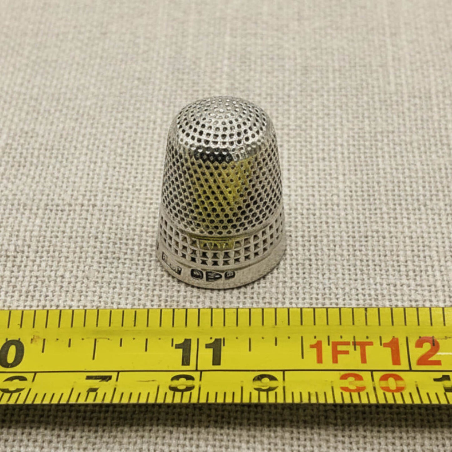 Silver thimble on a textured fabric background with a measuring tape for scale.