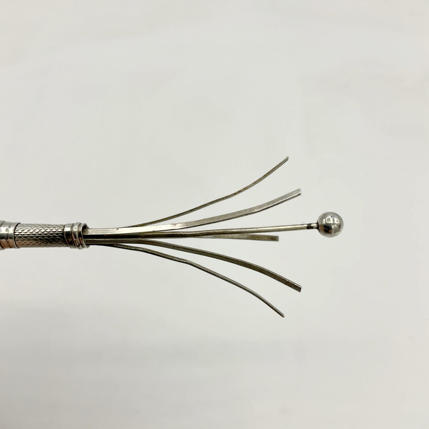 A close-up of a Art Deco Sterling Silver Cocktail Whisk against a plain light gray background.