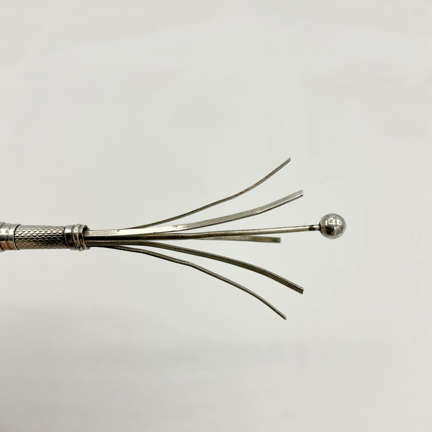 A close-up of a Art Deco Sterling Silver Cocktail Whisk against a plain light gray background.
