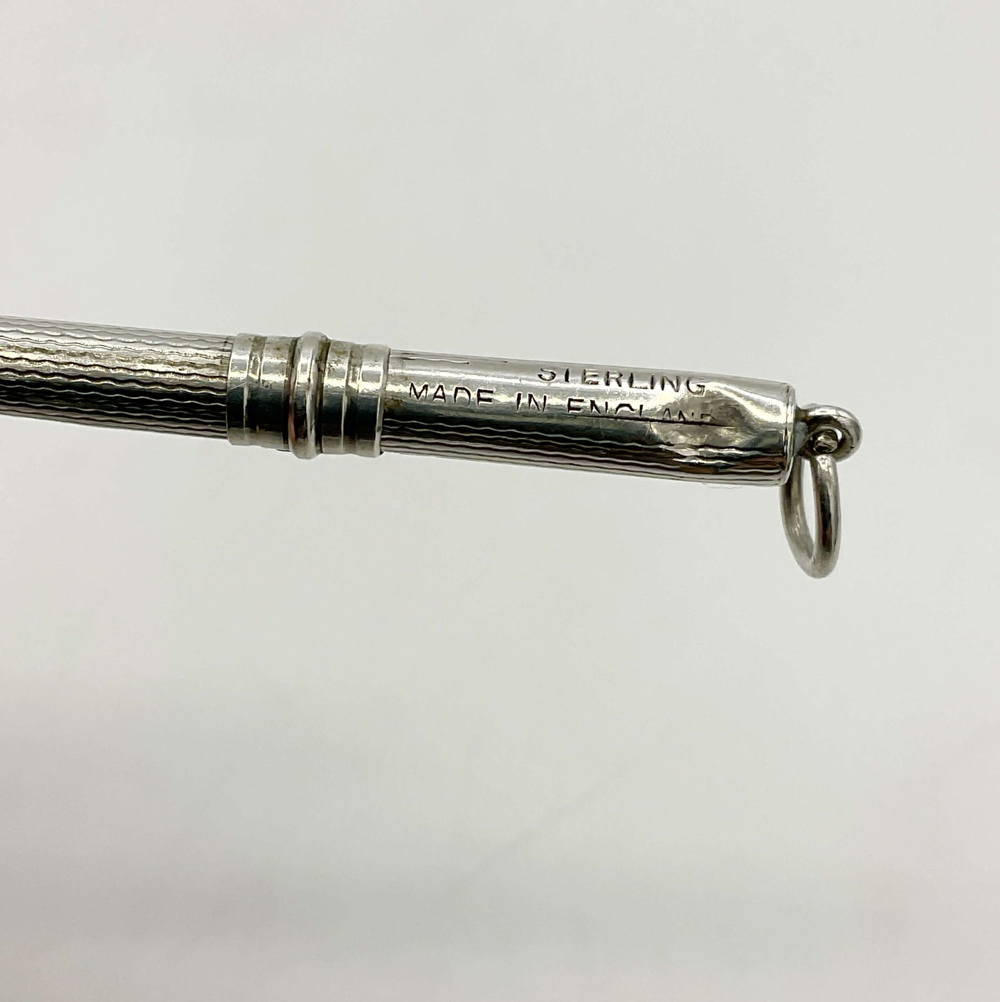 Close-up of a Art Deco Sterling Silver Cocktail Whisk engraved 'STERLING MADE IN ENGLAND', and a small hanging ring on a plain light gray background.
