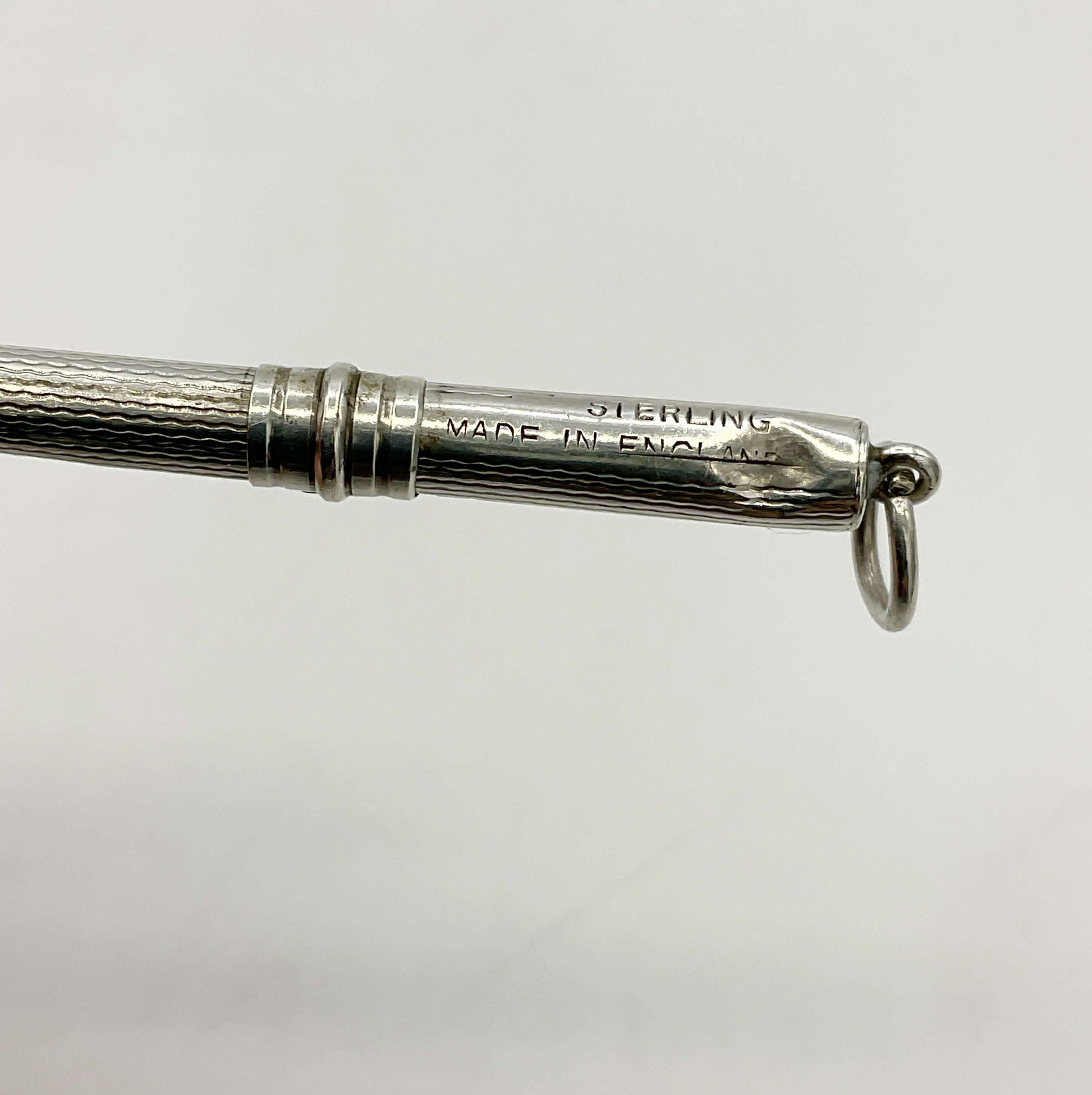 Close-up of a Art Deco Sterling Silver Cocktail Whisk engraved 'STERLING MADE IN ENGLAND', and a small hanging ring on a plain light gray background.
