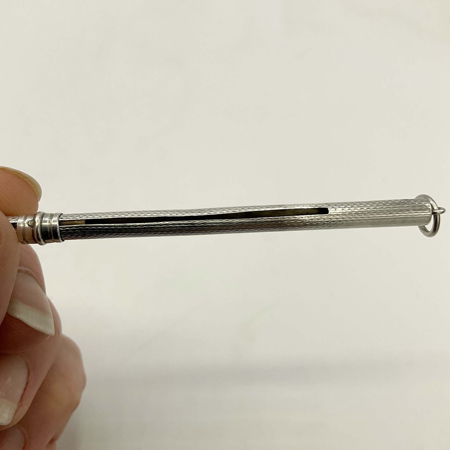 A close-up of Art Deco Sterling Silver Cocktail Whisk held horizontally by a hand against a plain light background.
