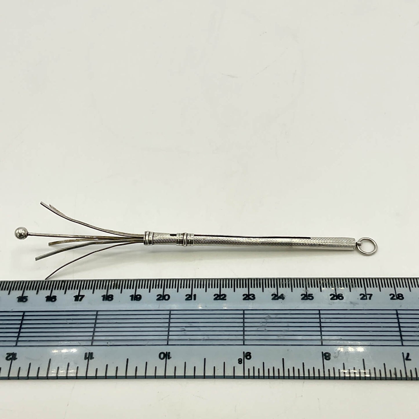 A Art Deco Sterling Silver Cocktail Whisk with multiple prongs and a small loop at the end, shown above a ruler for scale on a white background.