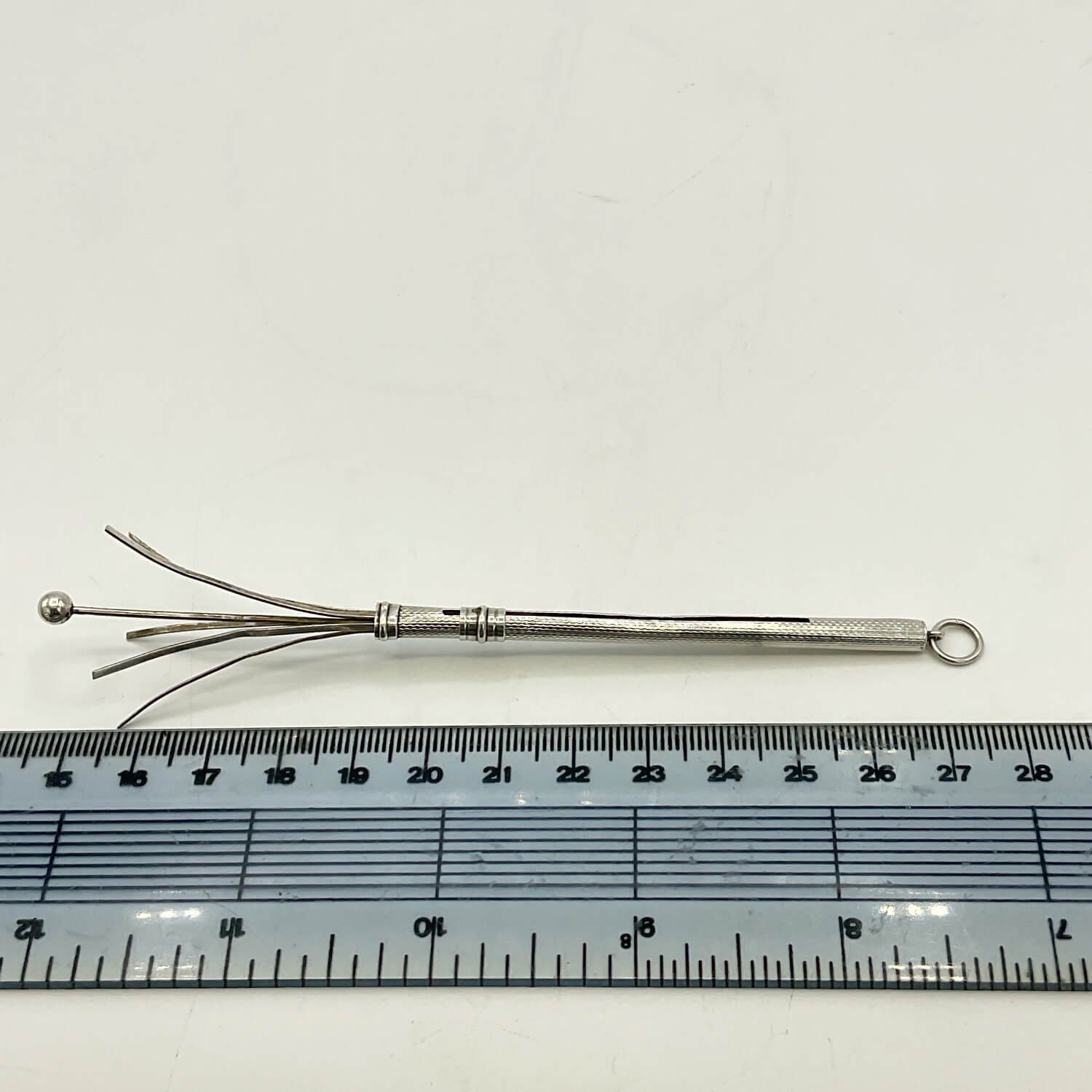 A Art Deco Sterling Silver Cocktail Whisk with multiple prongs and a small loop at the end, shown above a ruler for scale on a white background.