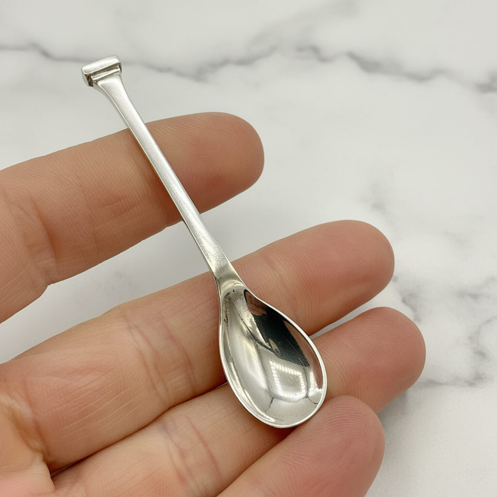 Silver salt spoon held between fingers against a marble background