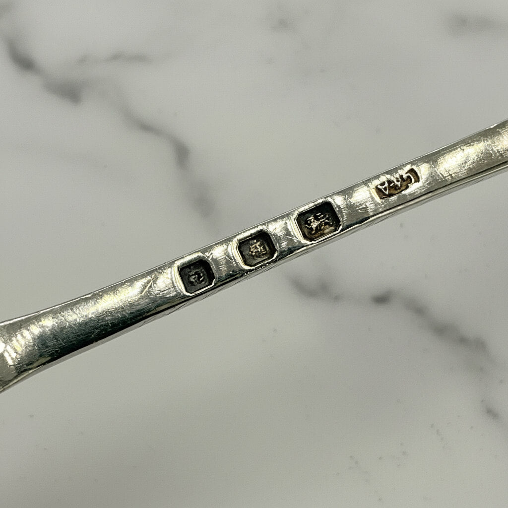 Close-up of hallmarks with engraved details on a silver salt spoon on a marble background