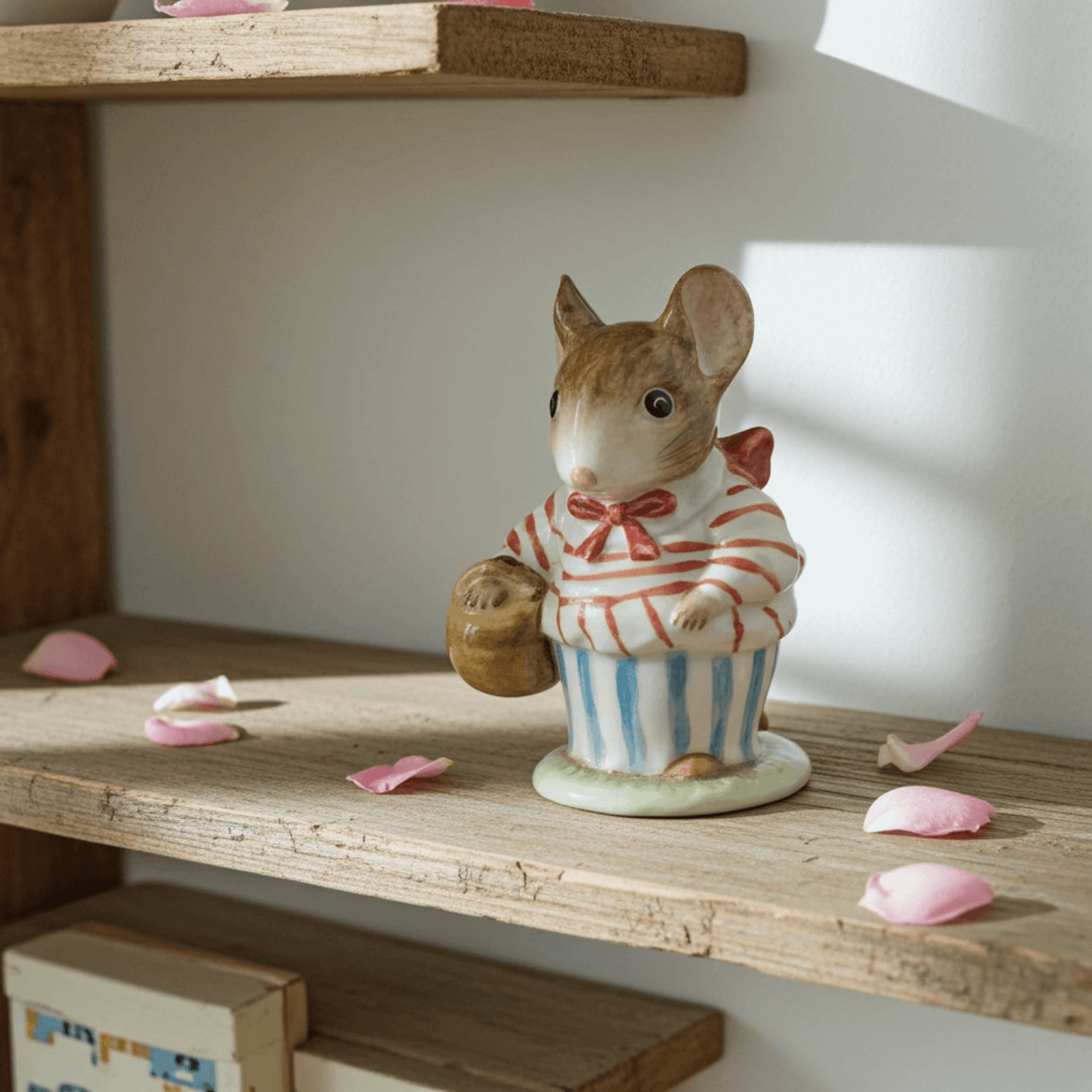Small figurine of a mouse in a striped outfit on a wooden shelf with pink petals.
