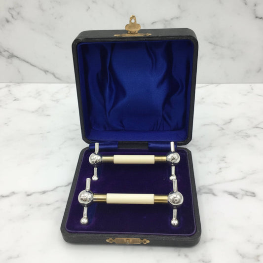 a pair of antique knife rests in a presentation box with gold-tone hardware, set against a white marble background.