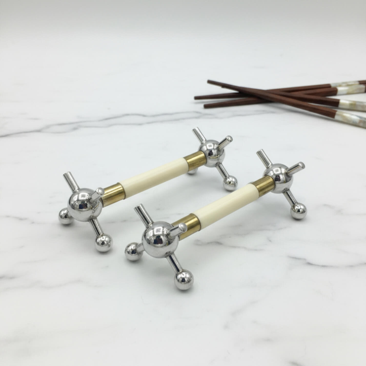 Pair of Antique Silver Plated Knife Rests with chopsticks in the background on a marble surface